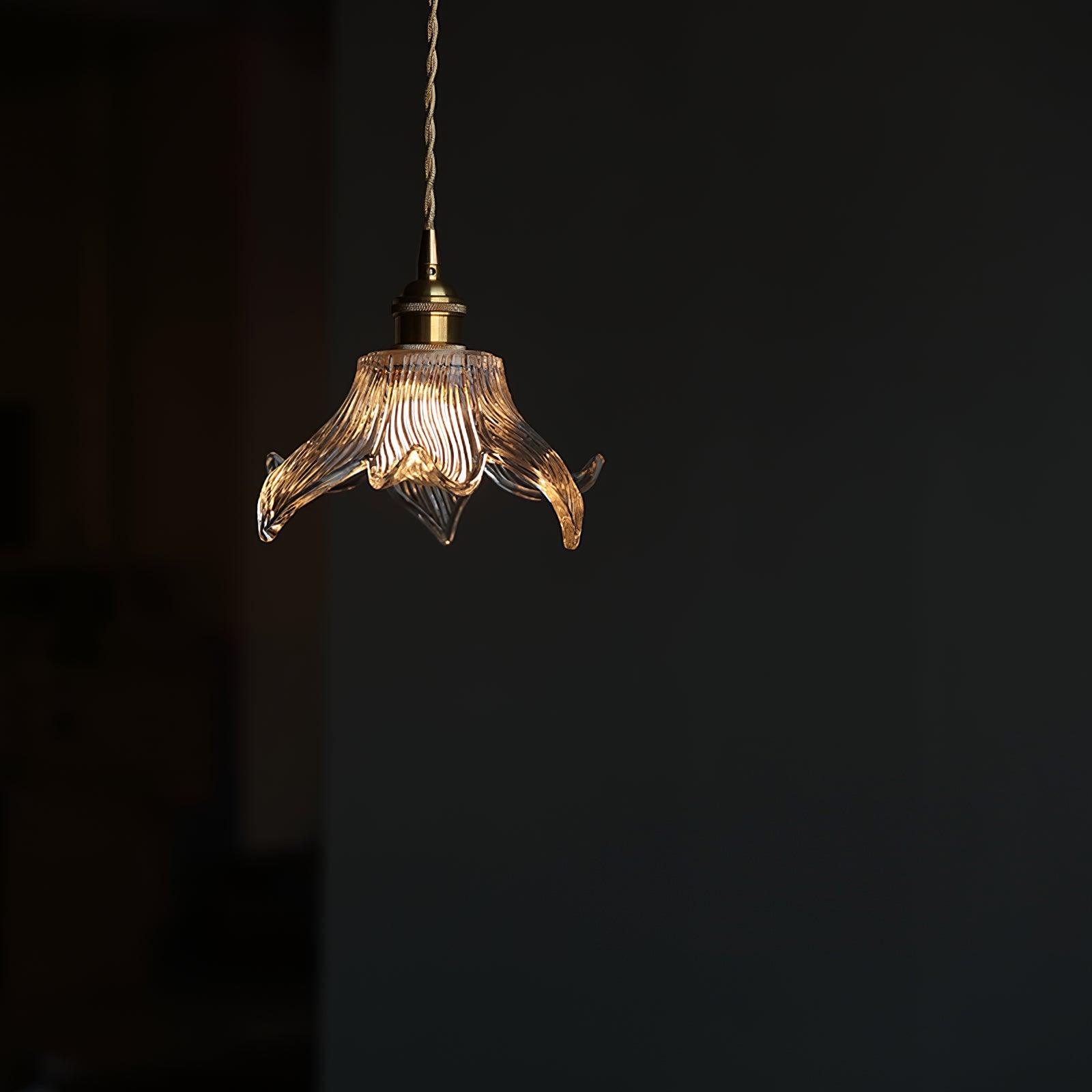 Clear petal pendant glowing in a dark room, with exposed round bulb and twisted suspension cord.