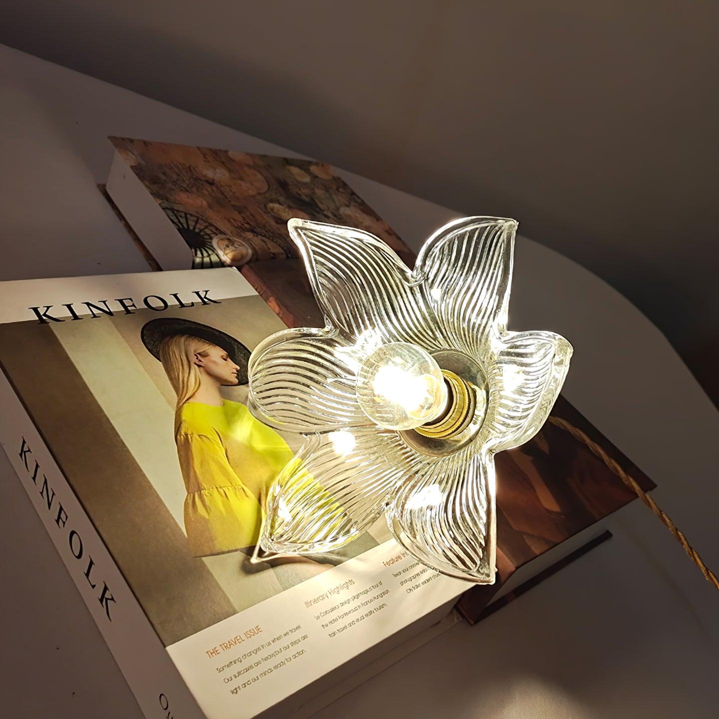 Underside of the lit flower glass pendant resting sideways on patterned books, with one clear round bulb at its centre.