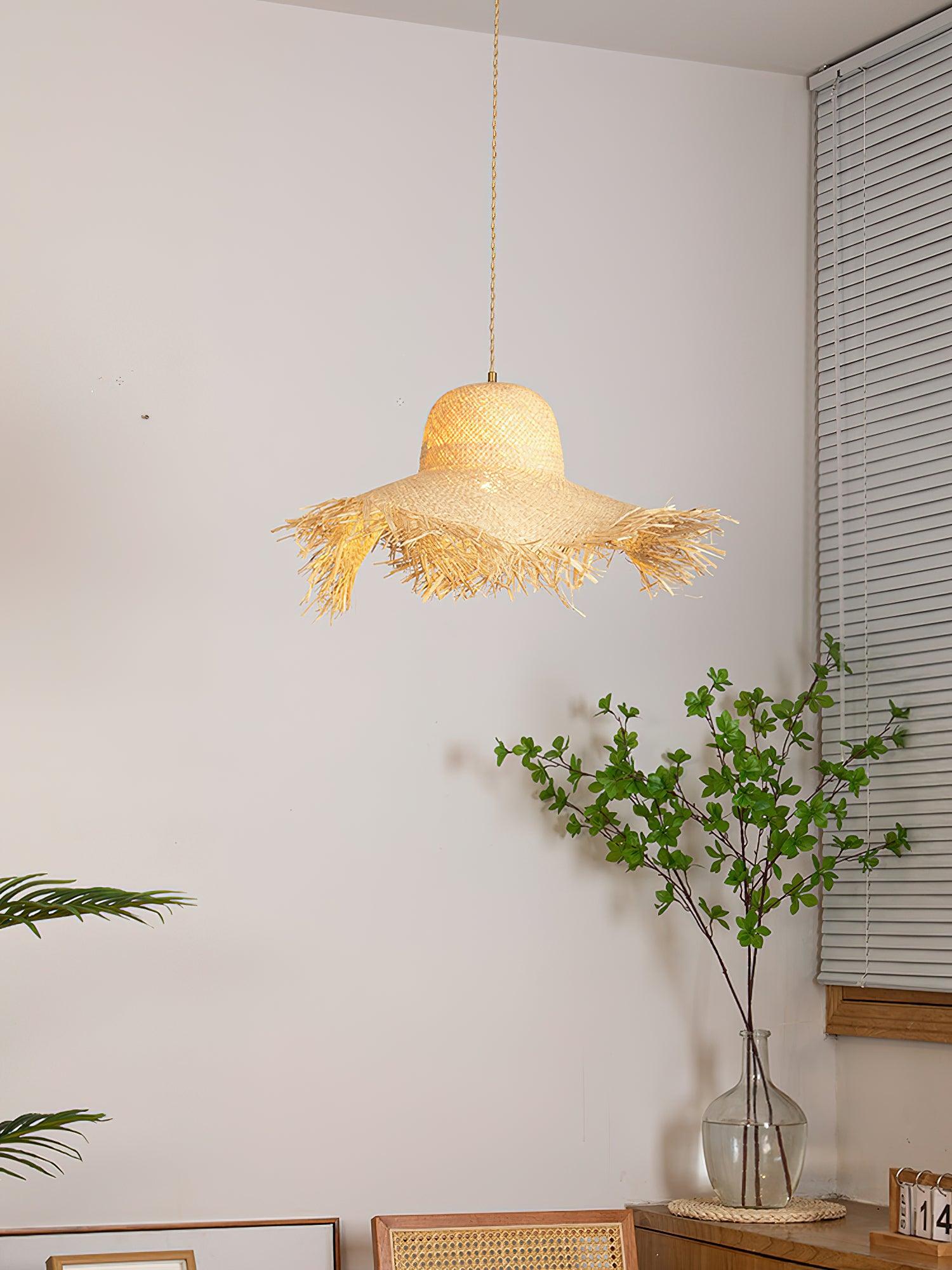 Rattan hat pendant by white window blinds above a cabinet with calendar, leafy vase and leaning frames