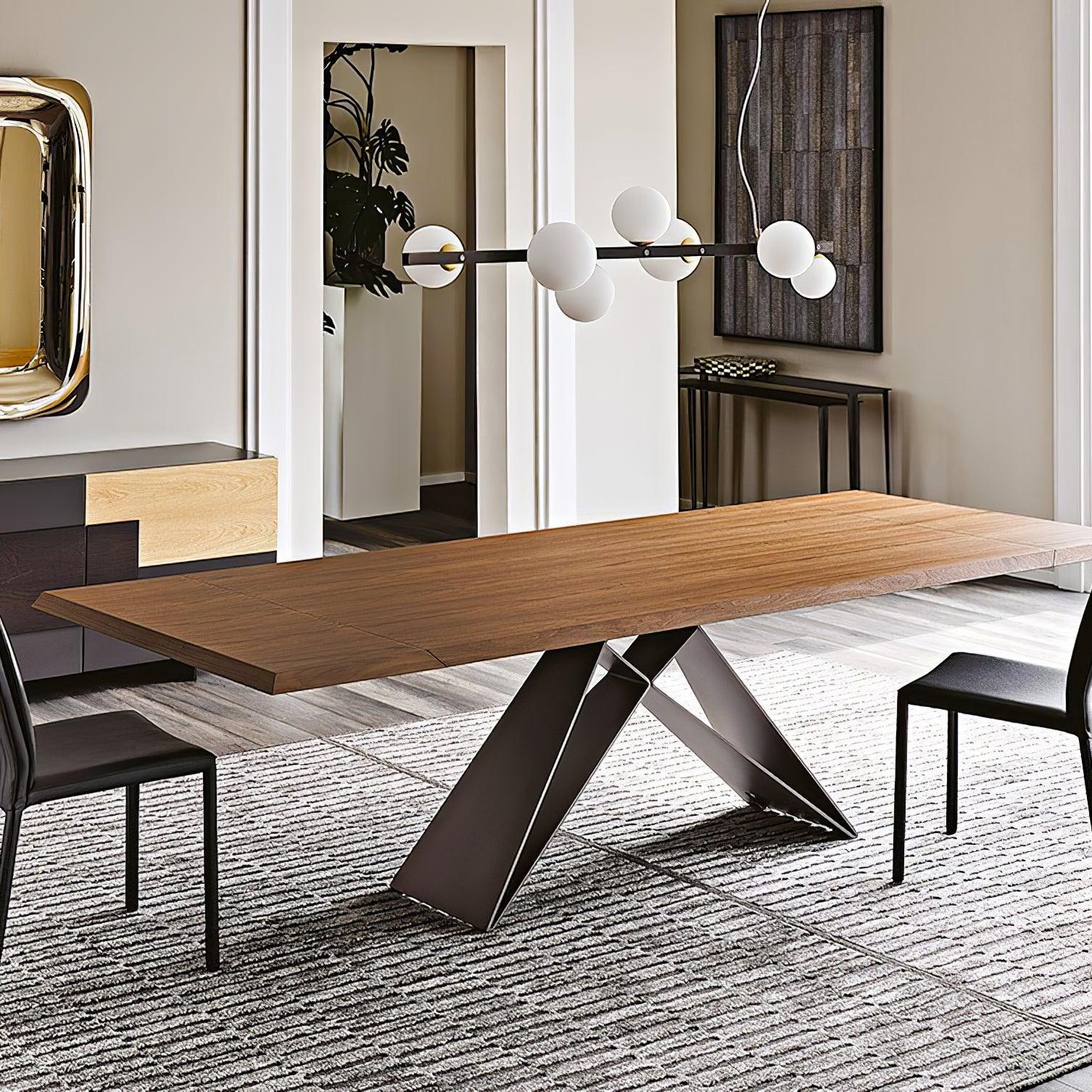 Globe pendant above long wood dining table and black chairs, beside gold-tone mirror, white moulding and doorway with leafy plant.