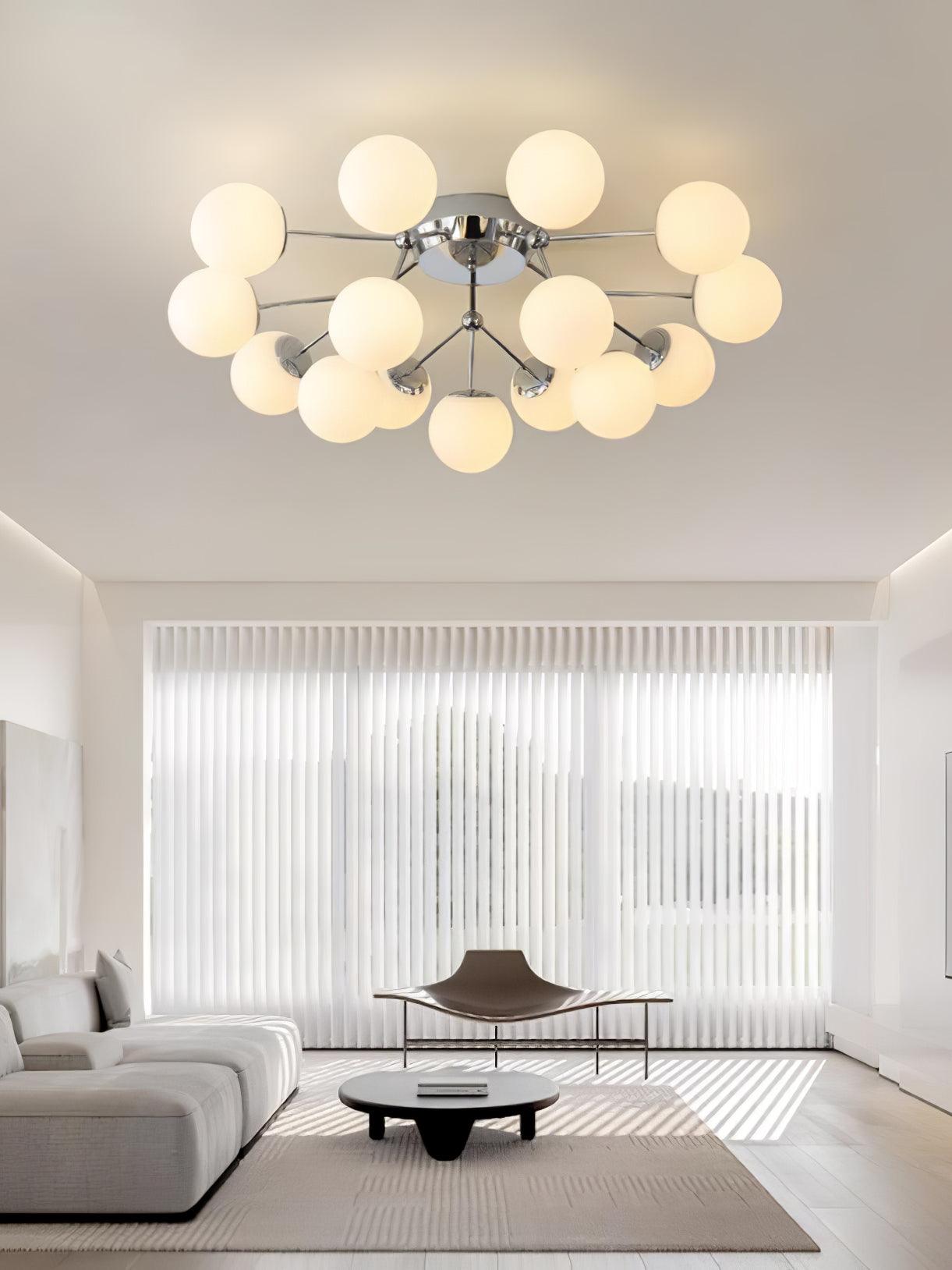 Warm-lit chrome globe ceiling cluster in a living room with pale sectional, low black table, sculptural bench and vertical blinds