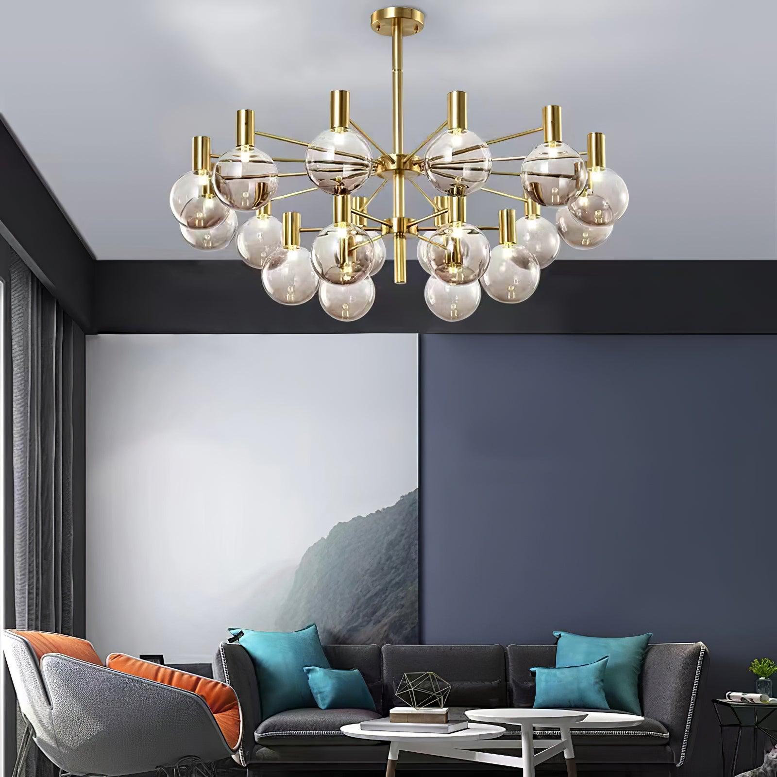 Two-tier clear-globe chandelier above a grey sofa and orange-cushion chair, with teal pillows and mountain artwork.