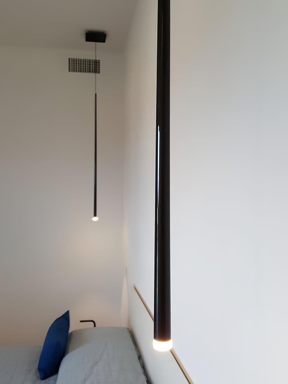 Close view of a glowing black tube pendant beside a grey bench, with a second single pendant behind