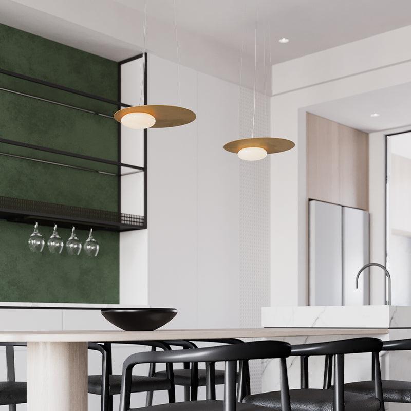 Two gold disc pendants over a pale table, black chairs and bowl, with green wall and wine-glass rack; sink island at right.