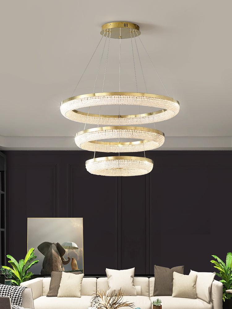 Three illuminated gold-rimmed crystal rings above a pale sectional sofa against a dark wall