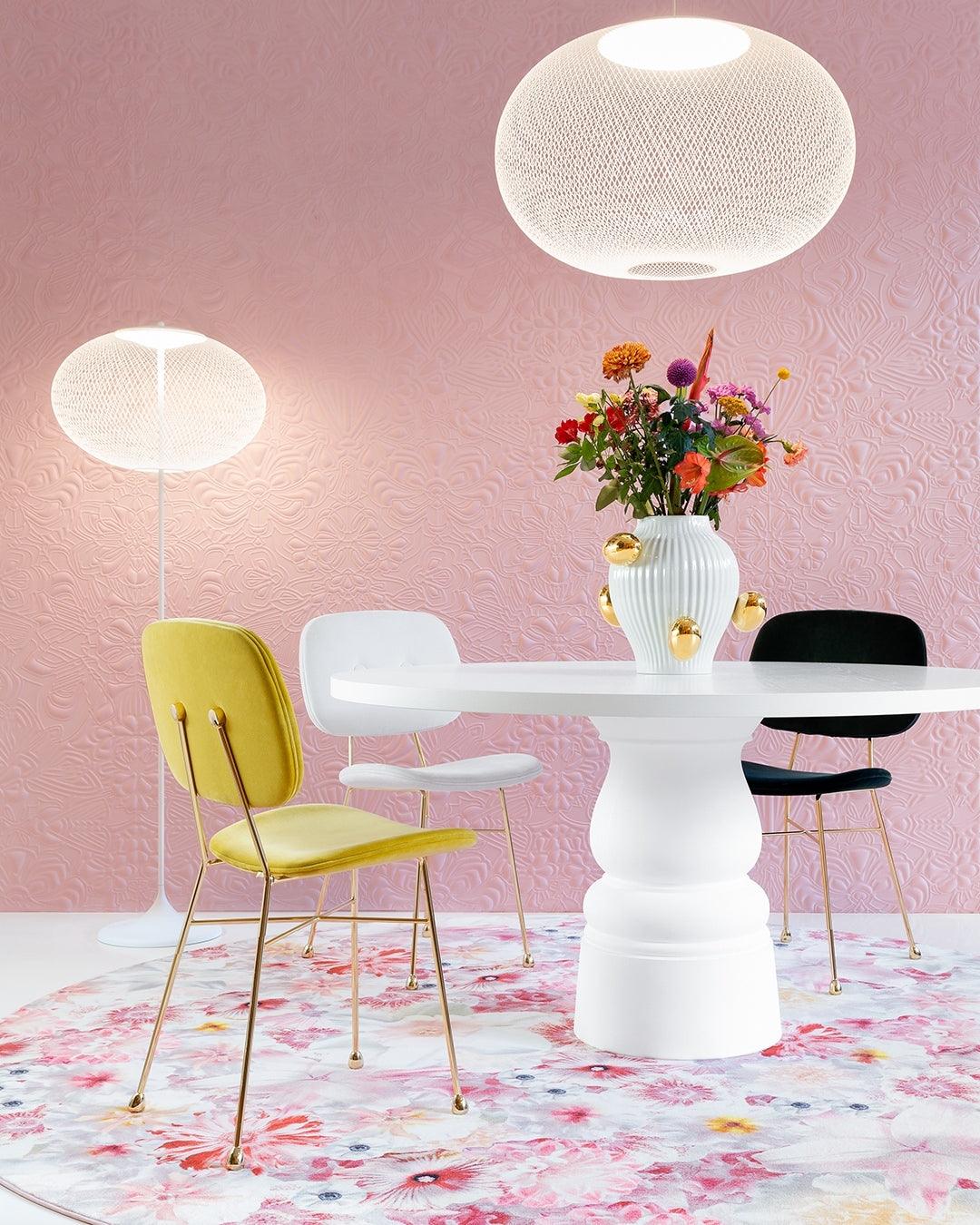 White mesh floor lamp behind a yellow dining chair beside a white table, with a separate large mesh pendant overhead