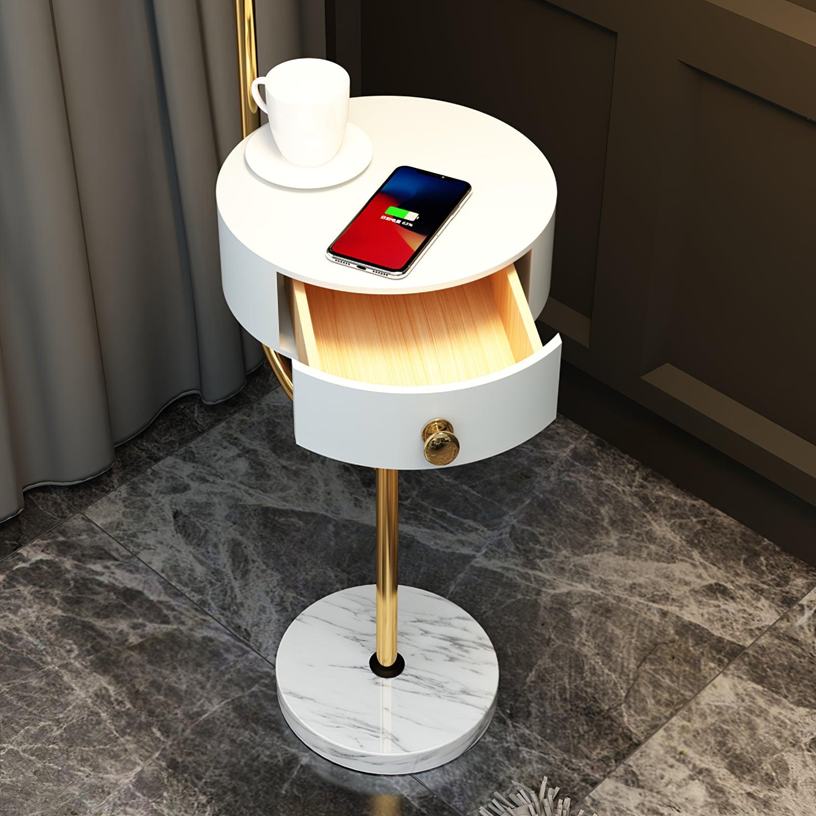 Close white round table with open curved-front drawer, pale wood interior and gold knob, cup and phone with charging-screen graphic