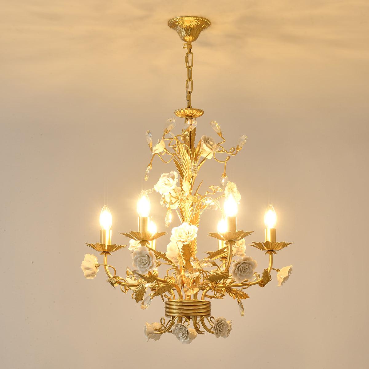 Square view of warm-lit rose chandelier with gold-tone canopy and chain against beige, white roses and leaf-shaped cups