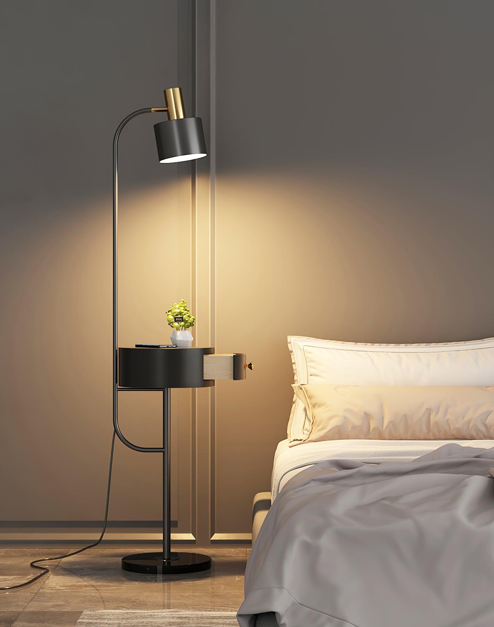 Black lamp lit beside white bed, black shade and open drawer table with phone and plant, gold fitting and dark round base