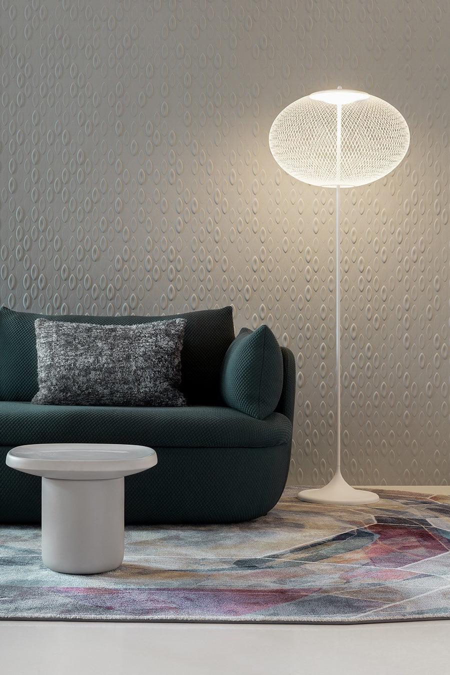 White mesh floor lamp beside a dark green sofa and low white table against a pale textured wall