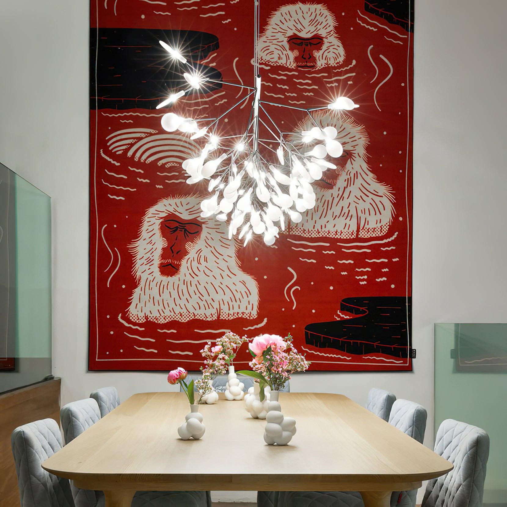 End-on chandelier view over wooden dining table, grey chairs and flower vases, against large red monkey artwork