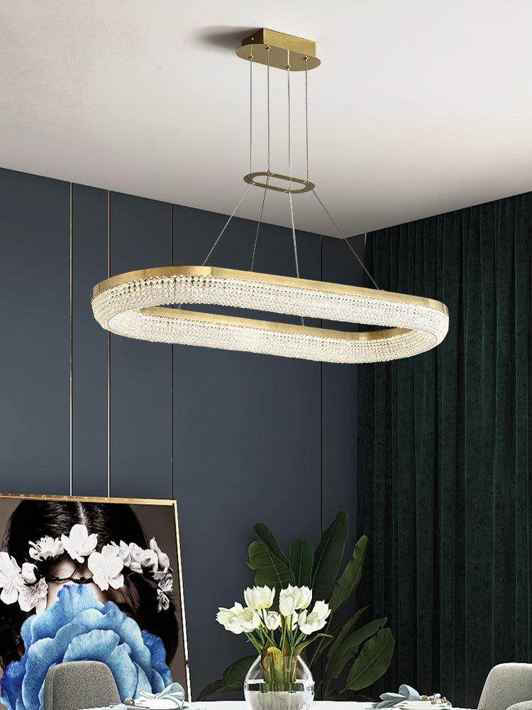 Elongated oval crystal chandelier with gold rim above a dining setting with flowers and dark walls
