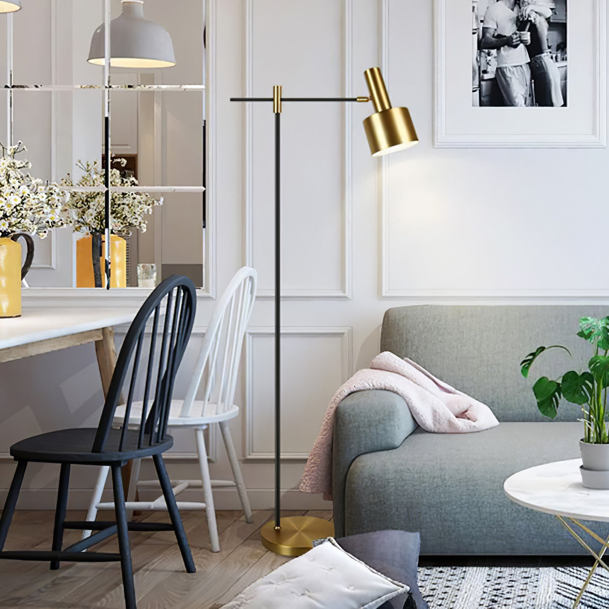Lit black and gold floor lamp beside grey sofa with pink throw and framed photographs on the wall