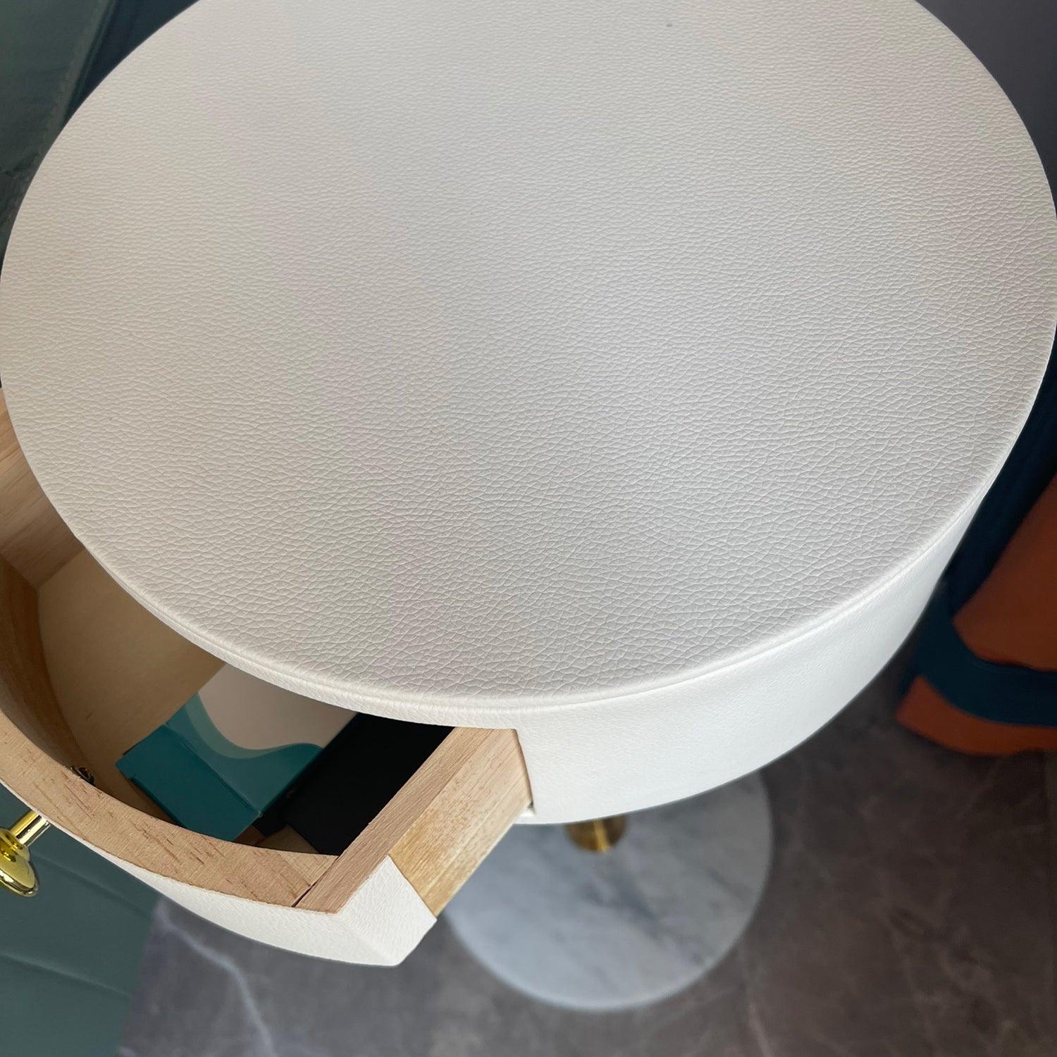 Close white textured tabletop with open pale wood drawer containing small objects, gold knob and veined base below