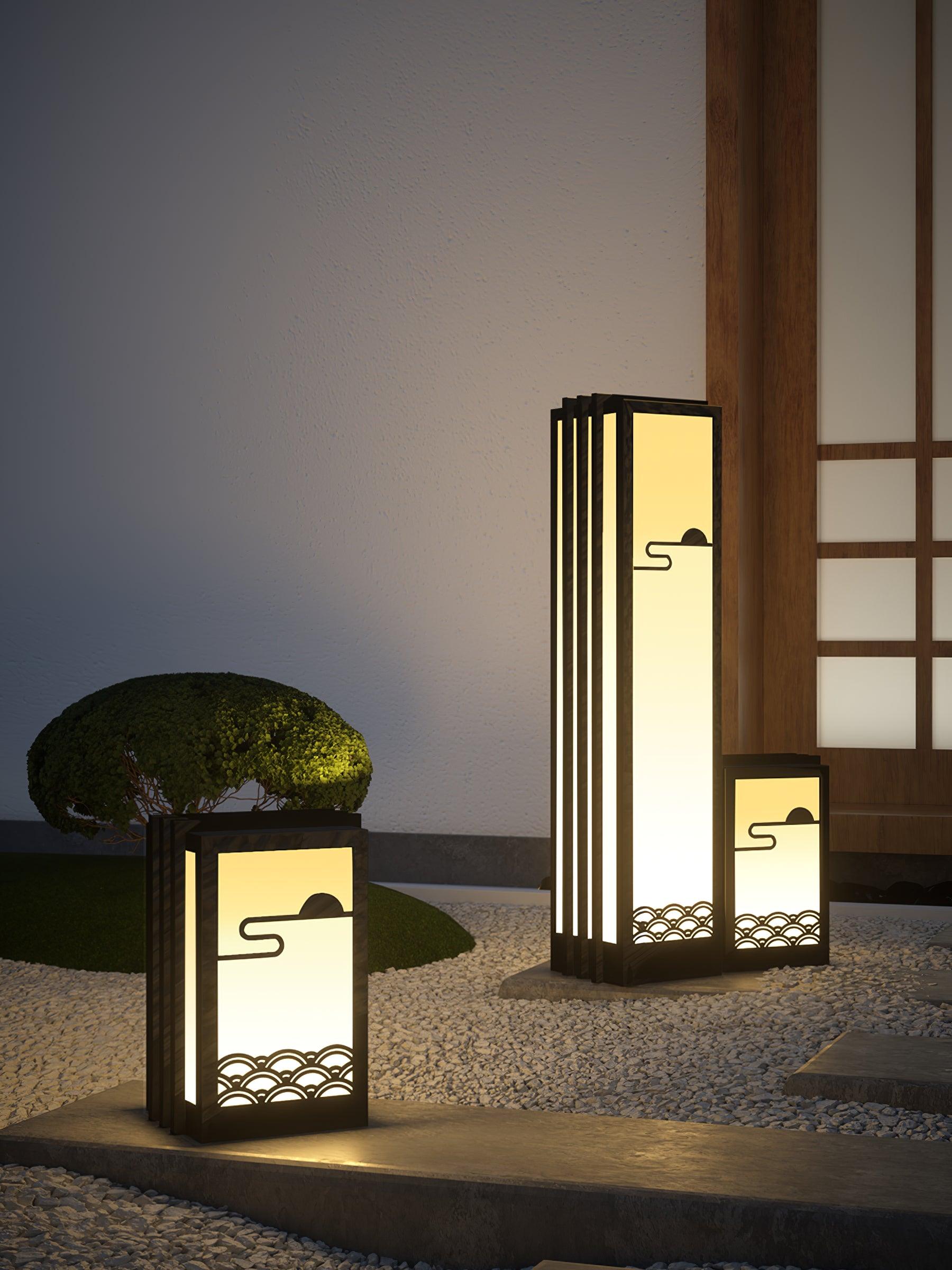 Vertical entrance composition with three lit lanterns, gravel, rounded shrub, paving and wood-grid door