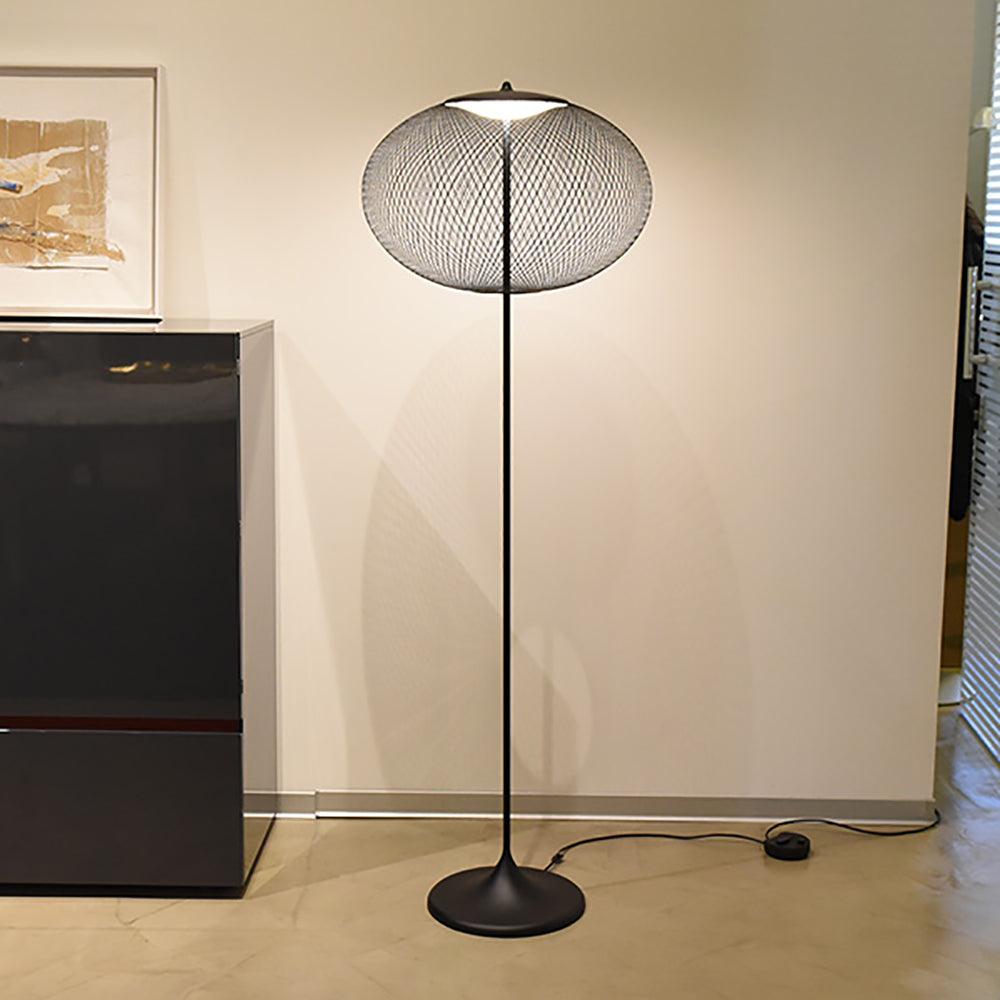 Black mesh floor lamp beside a dark cabinet, with its cord and circular inline switch visible on the wood floor