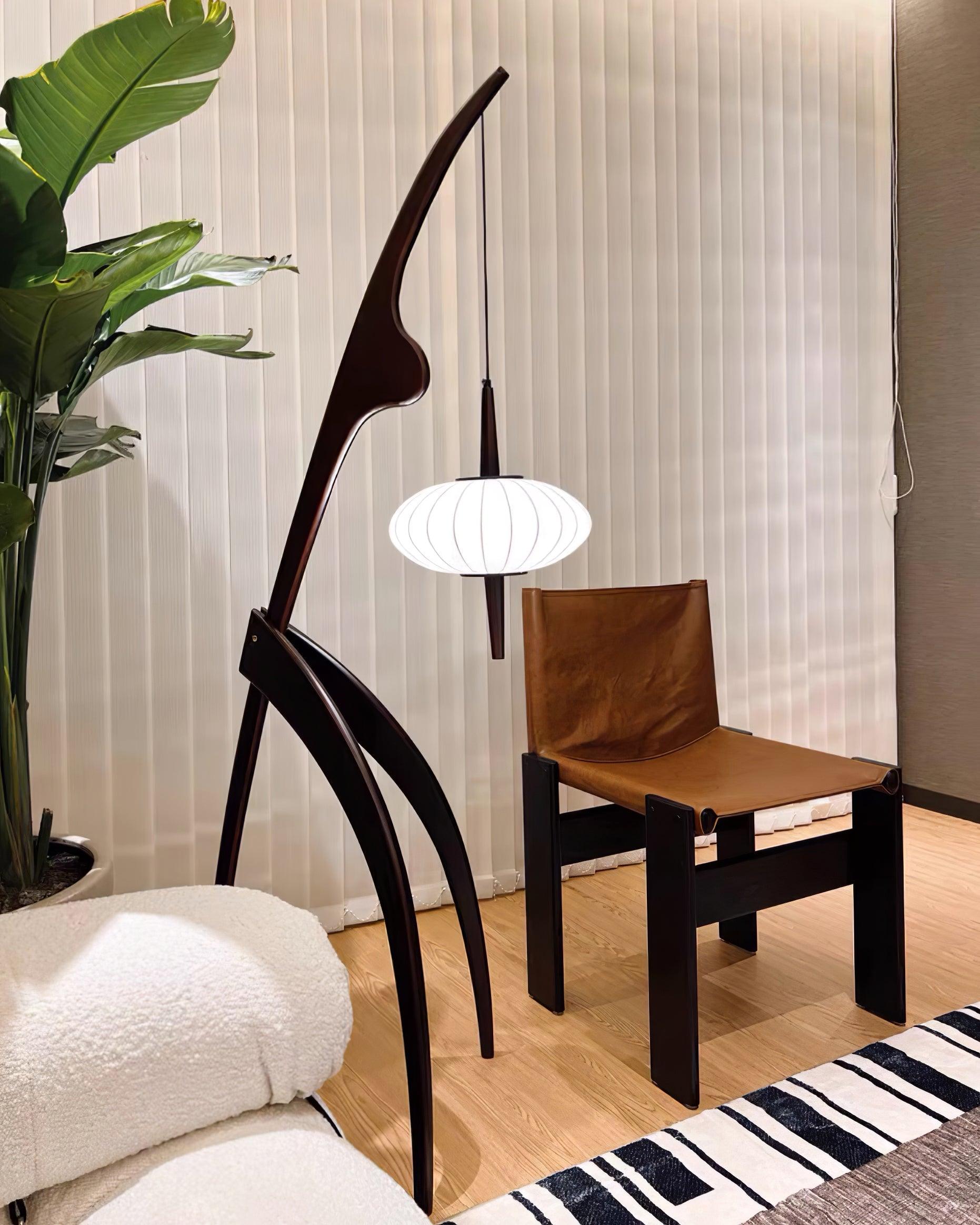Dark wood Mantis sculptural floor lamp near a wooden chair and bed