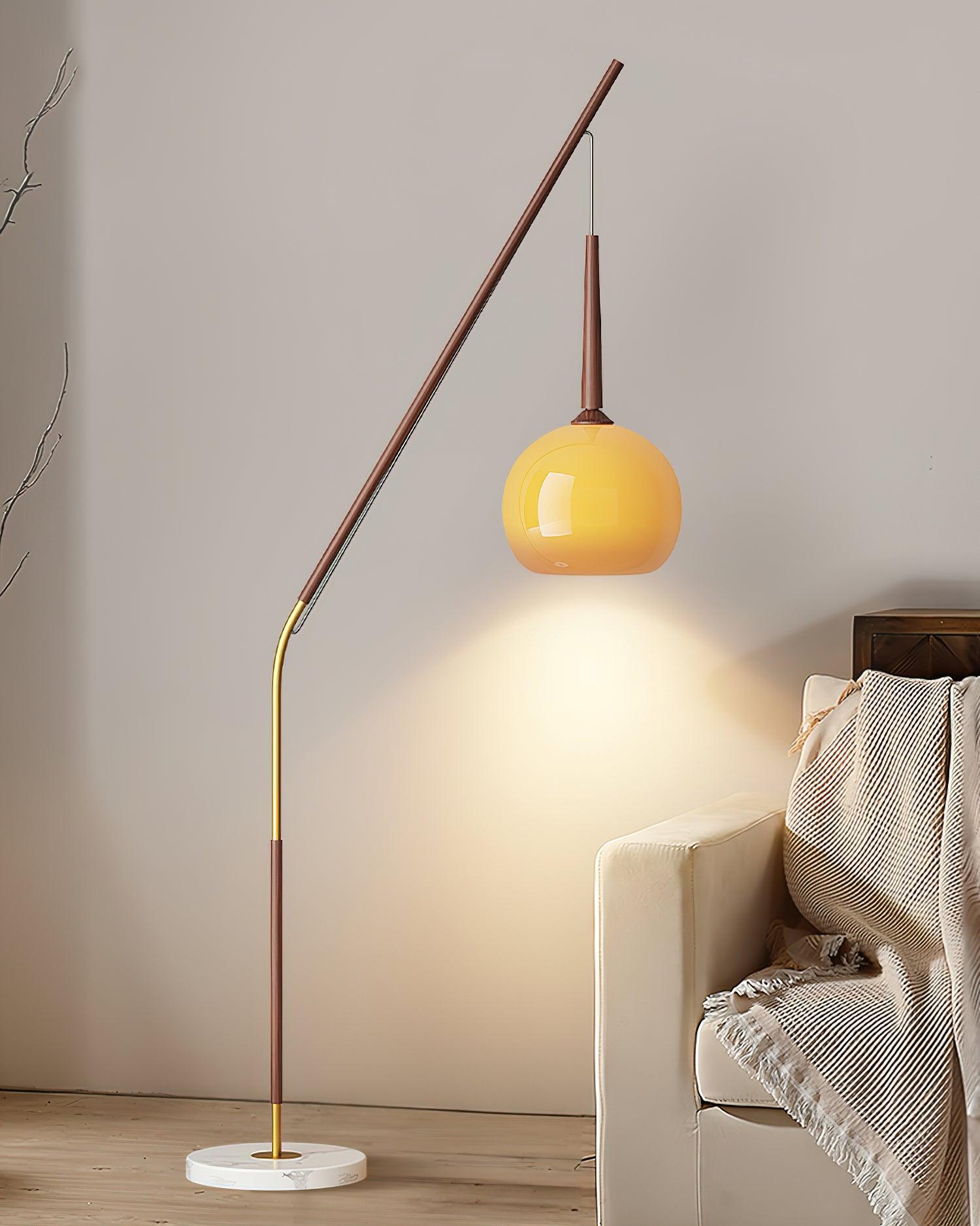 Dark wood-colour lamp with its orange shade hanging left beside a cream sofa, dried flowers and round coffee table