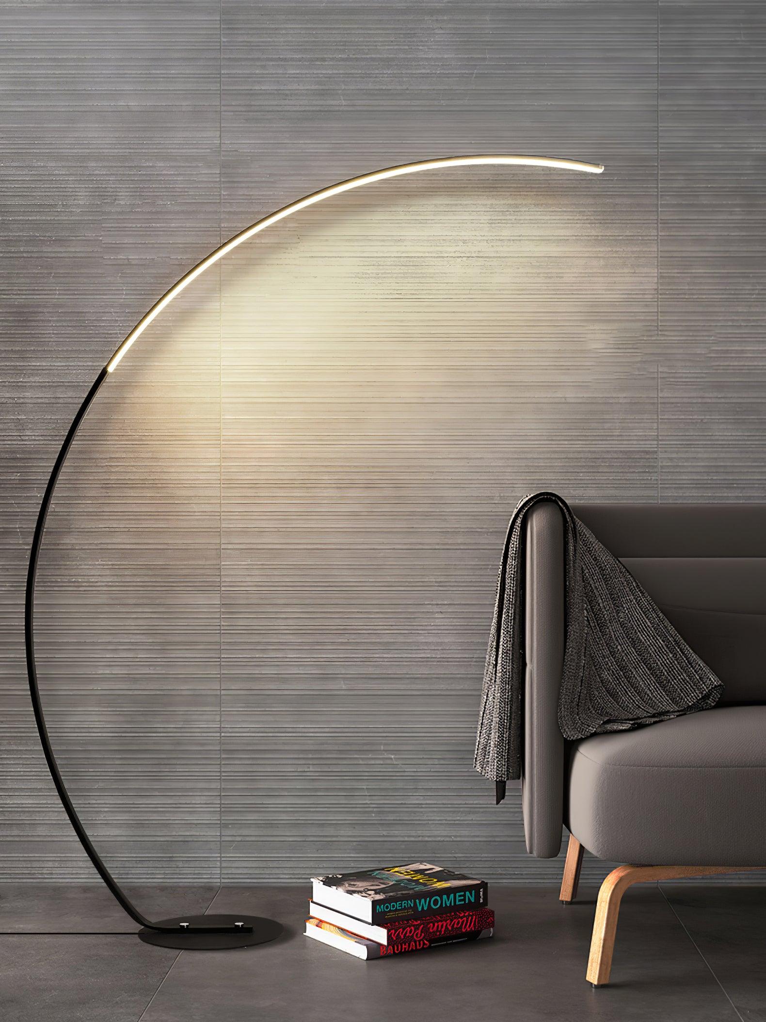 Vertical view of Black Arc floor lamp beside dark chair with draped throw and book stack against textured grey wall