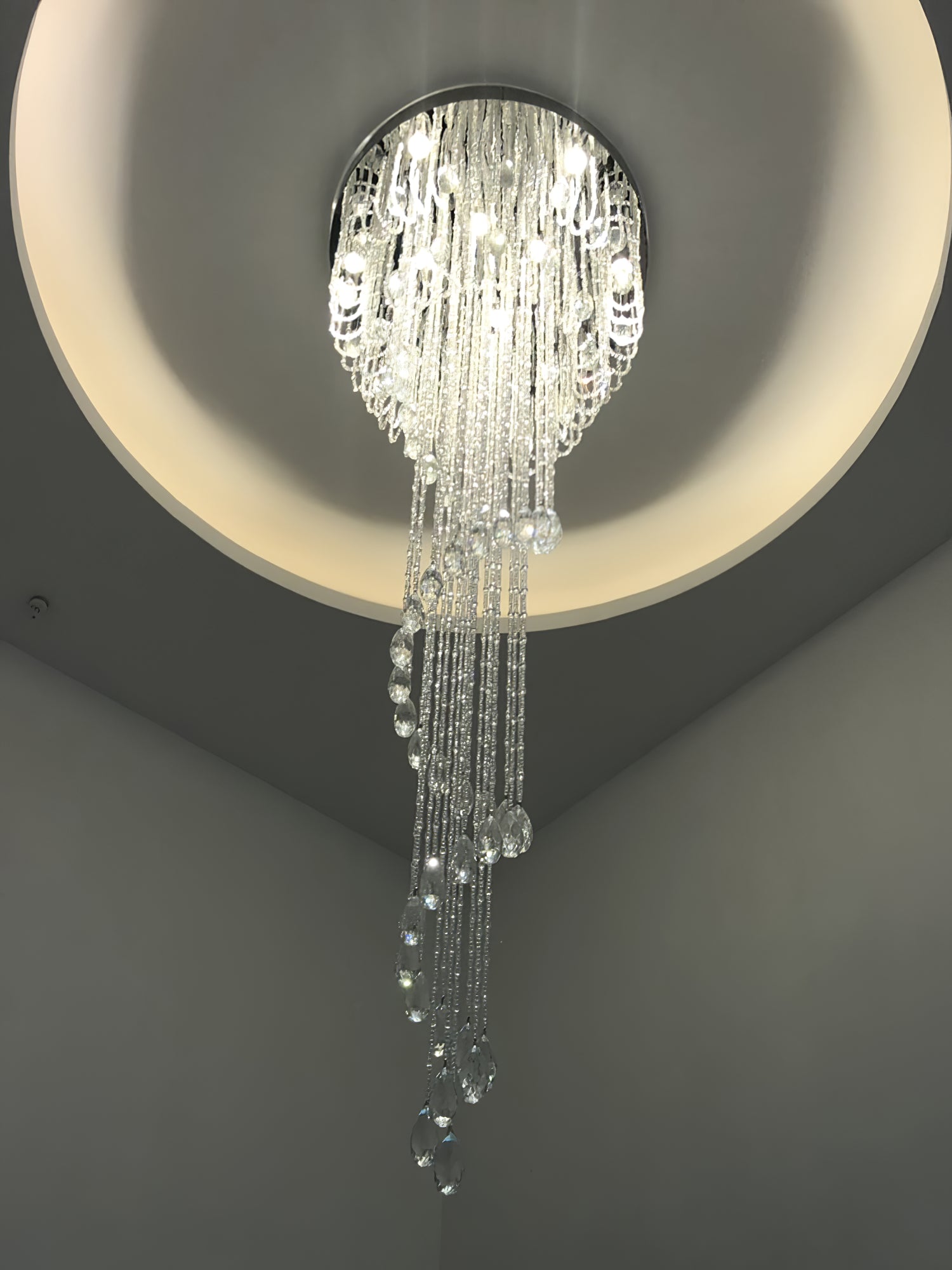 Upward view of lit crystal spiral under a separate circular ceiling recess with surrounding warm cove light