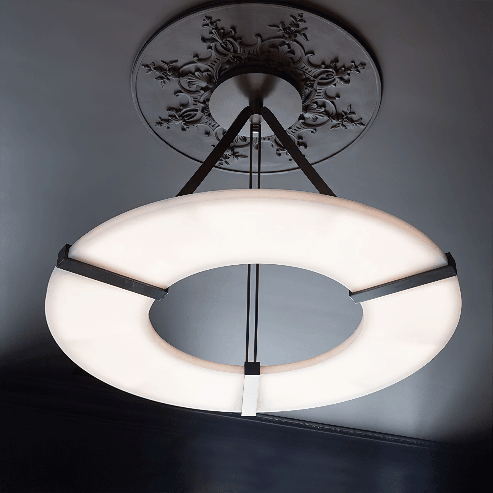 Low underside view of white halo ring and black supports below an ornate ceiling medallion