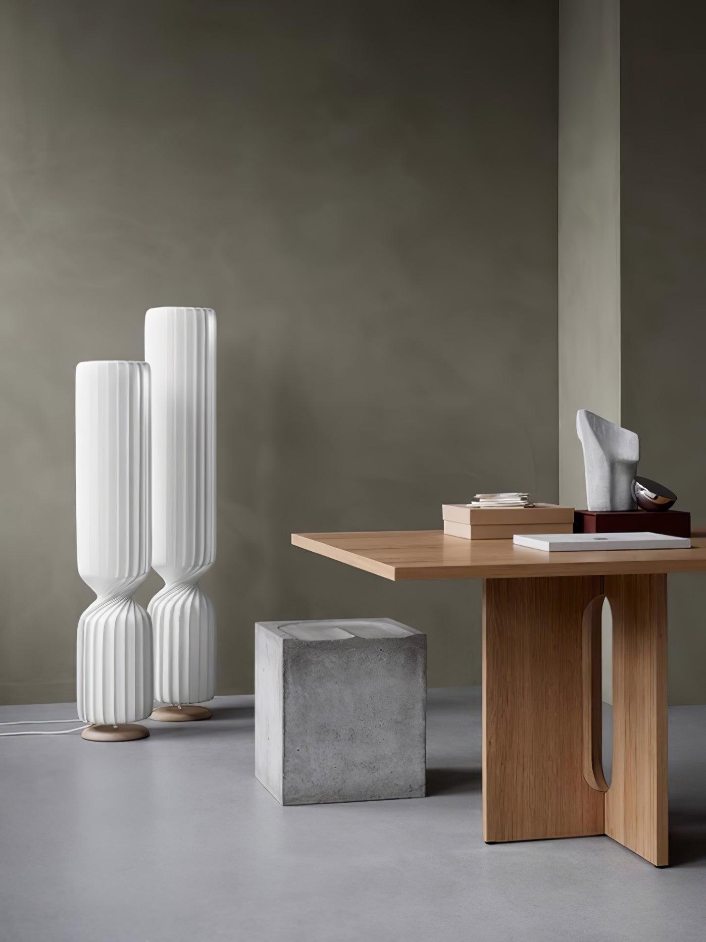 Wide vertical view of two white twist lamps beside wooden console with books and sculpture, gray block stool and floor cords