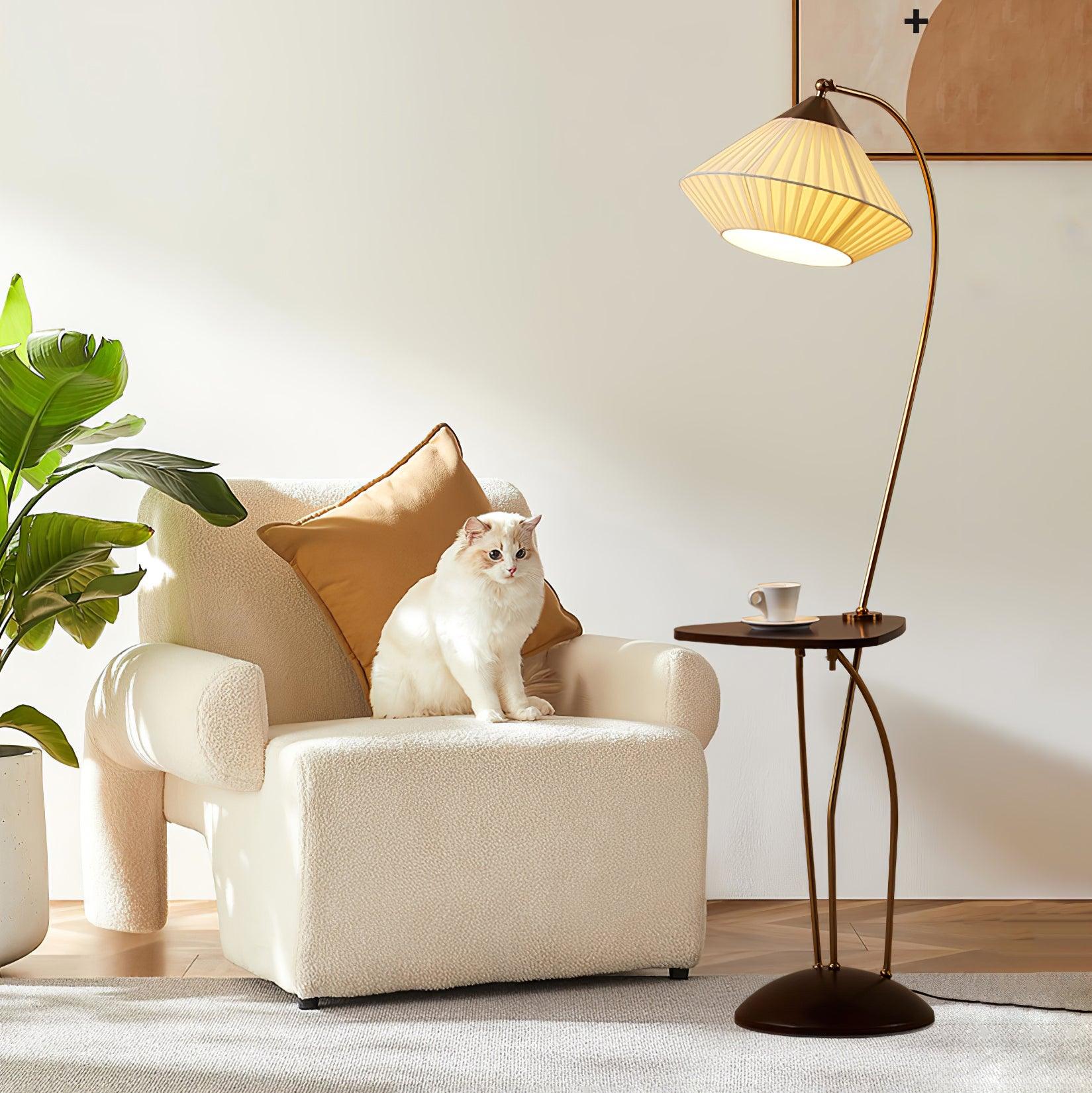 Lit Curve lamp and cup-topped table beside a cream armchair with a cat, ochre cushion and broad-leaf plant