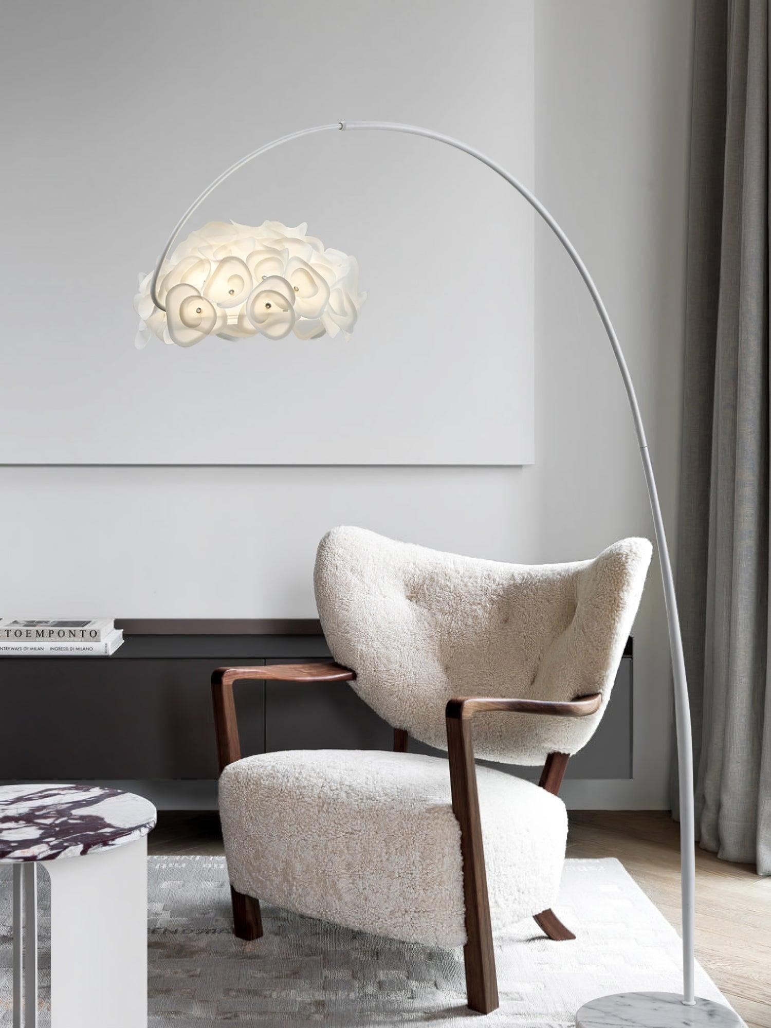 Arched white petal lamp over cream wooden-arm chair, gray curtain, dark cabinet with books and partly cropped veined base