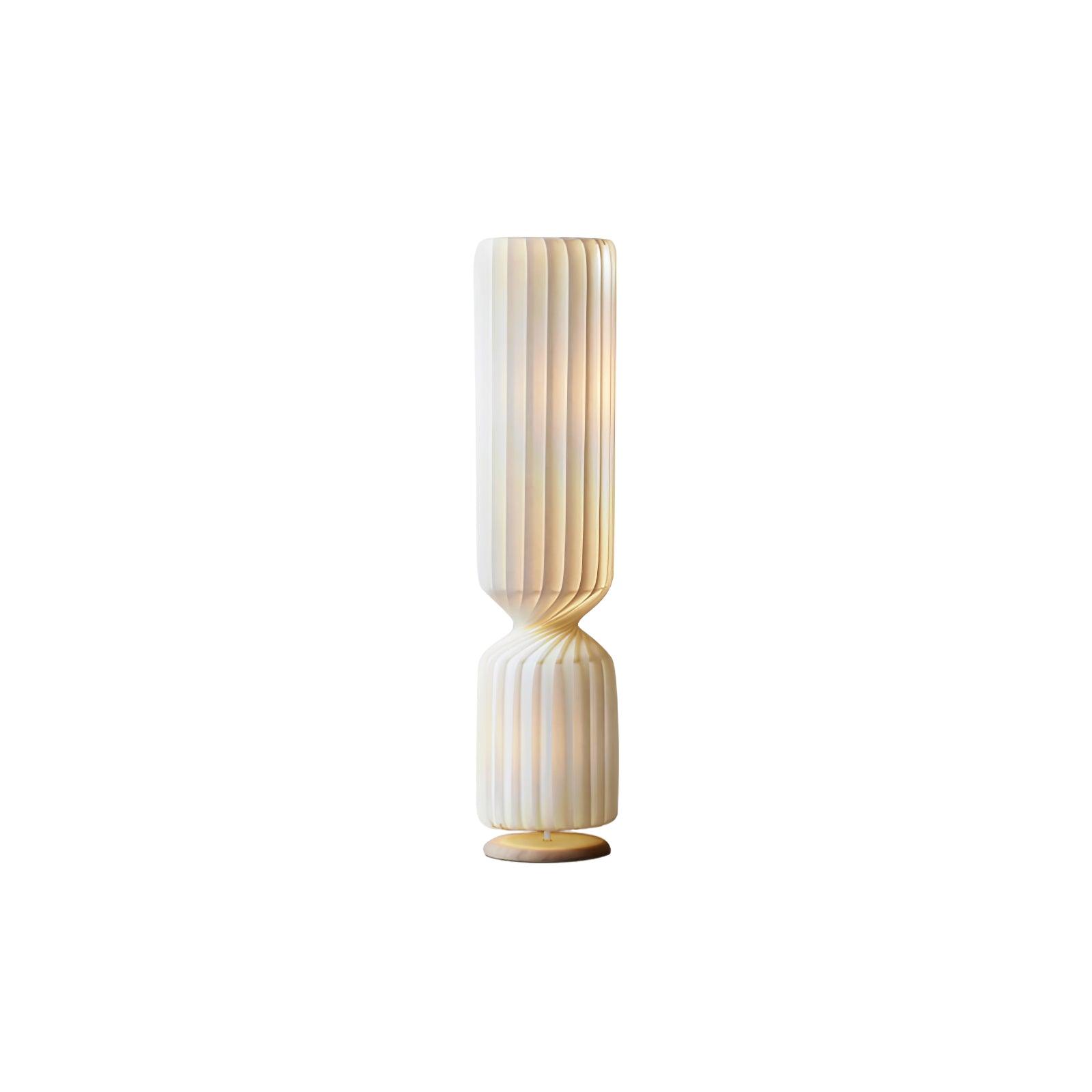 Isolated lit-looking white pleated twist lamp on white, with narrowed waist, shorter lower section and pale gold-toned base