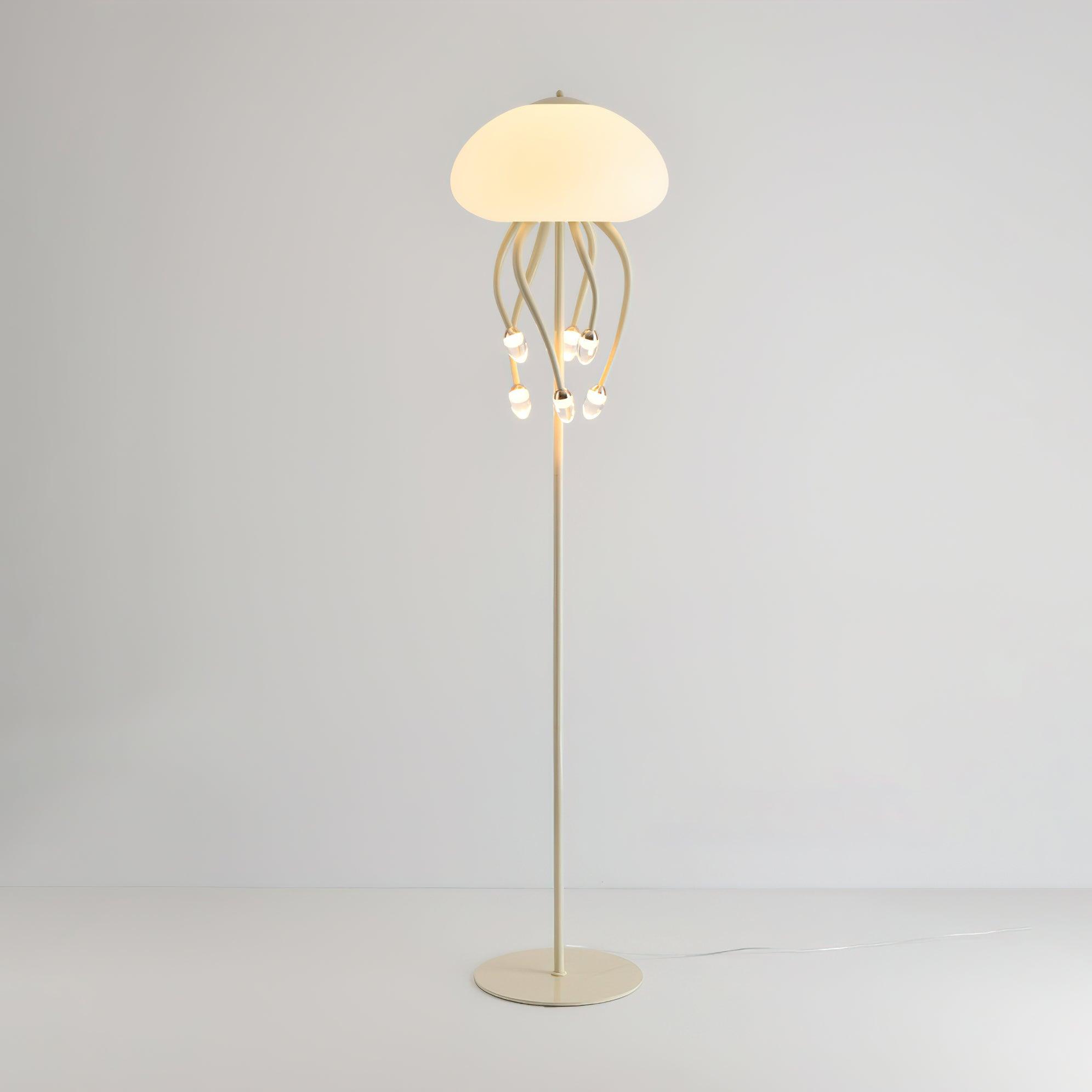 Beige six-arm Jellyfish floor lamp against pale wall and floor, with glowing dome and cable extending to the right.