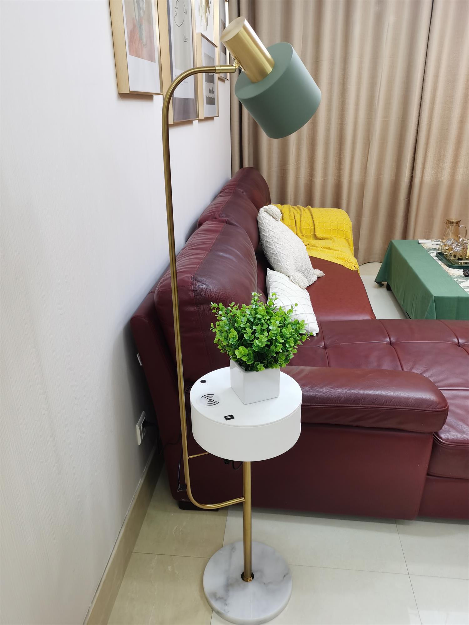 Gold lamp beside burgundy sofa, green shade, white closed-drawer table with plant and phone, symbol on tabletop and white base