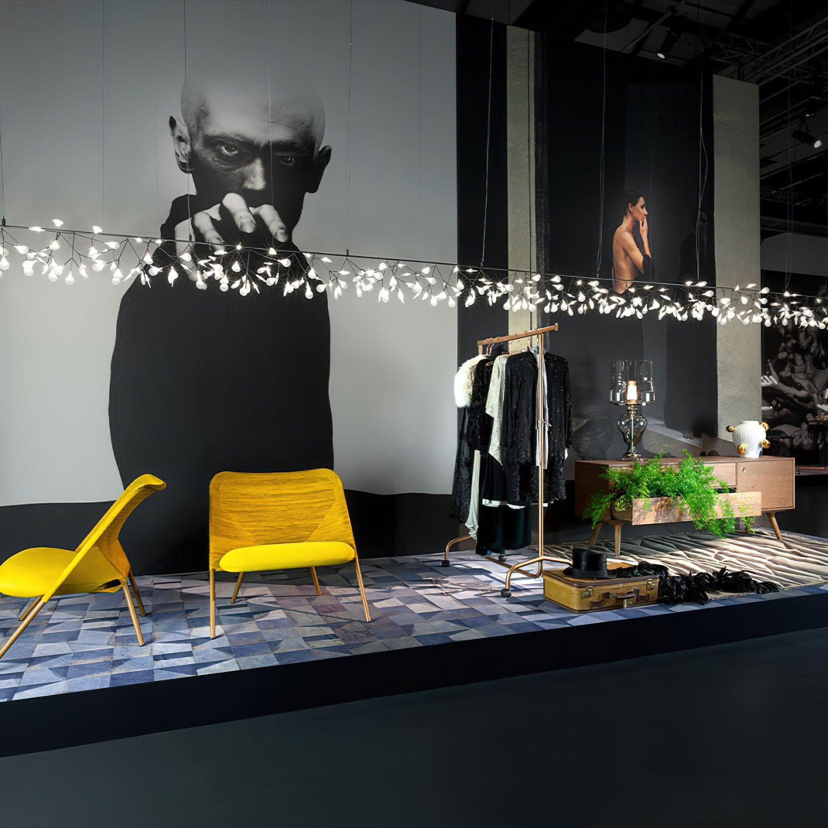 Long illuminated petal chandelier across showroom with yellow chairs, clothing rack and large portrait prints