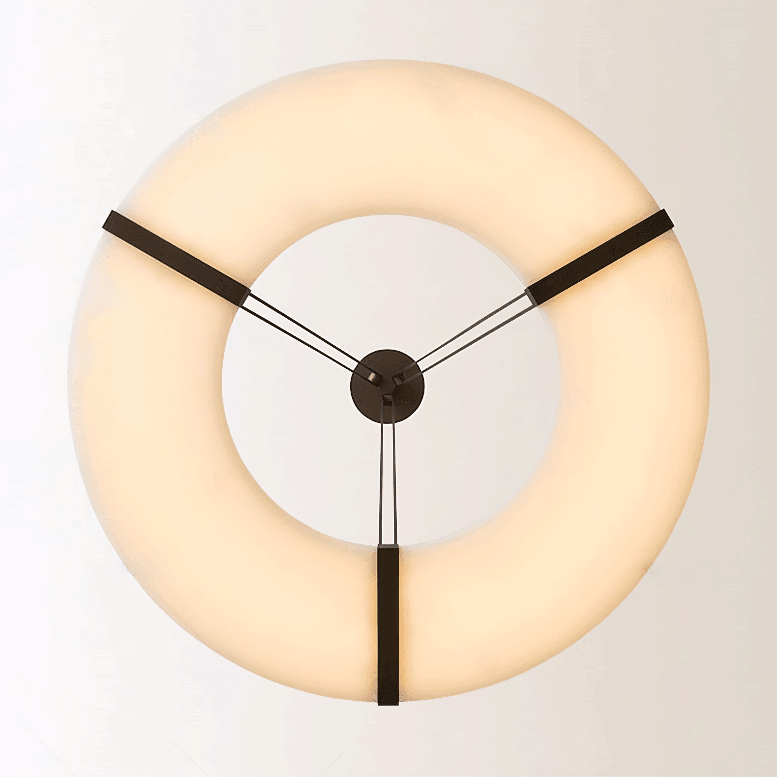 Underside of glowing cream halo ring with open centre and three black brackets against a pale ceiling