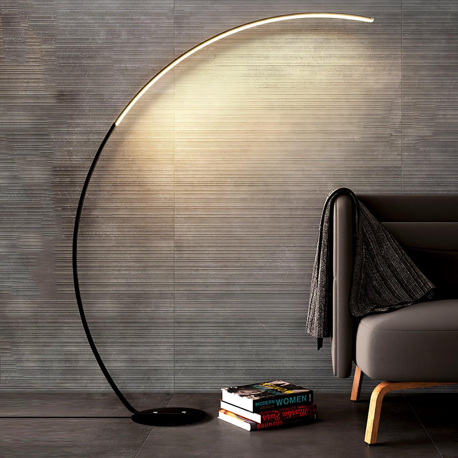 Black lit Arc floor lamp beside dark chair with draped throw and stacked books, against textured grey wall