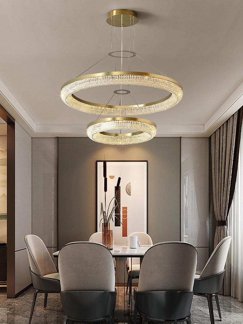 Two-tier crystal ring chandelier above a dining table and pale chairs beside curtains