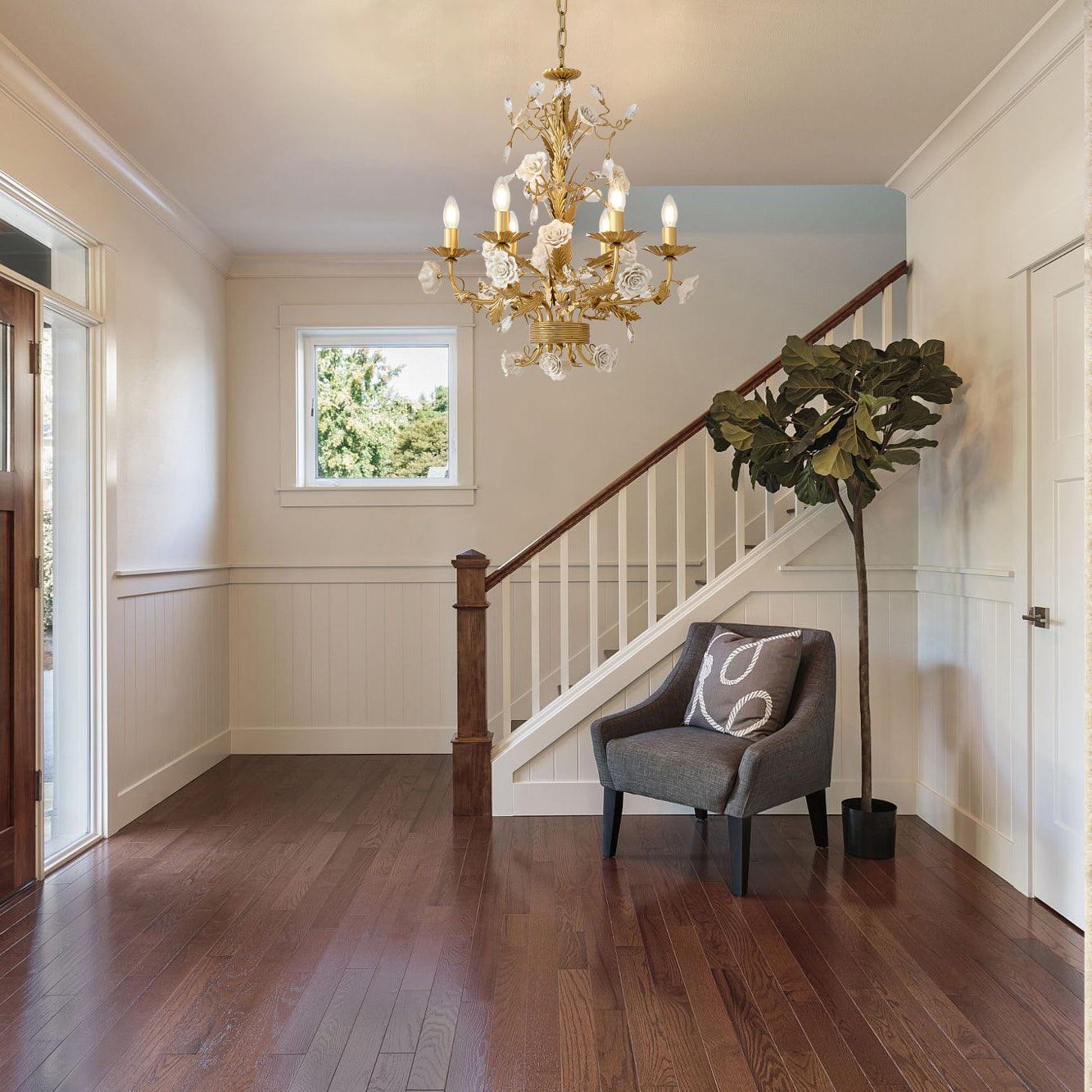 Lit White Rose chandelier in a paneled stair hall with dark wood rail and floor, gray chair and tall green plant