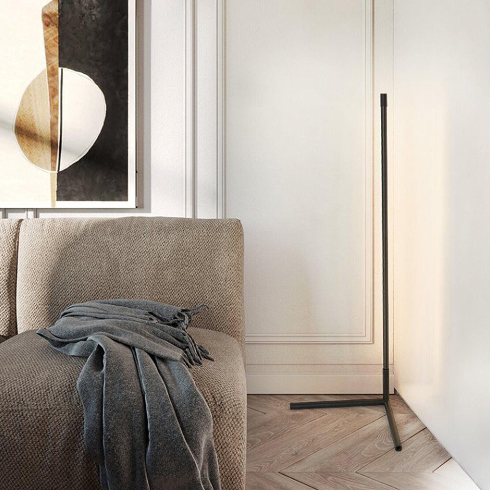 Black corner lamp behind a fabric sofa with grey throw, beside geometric framed artwork