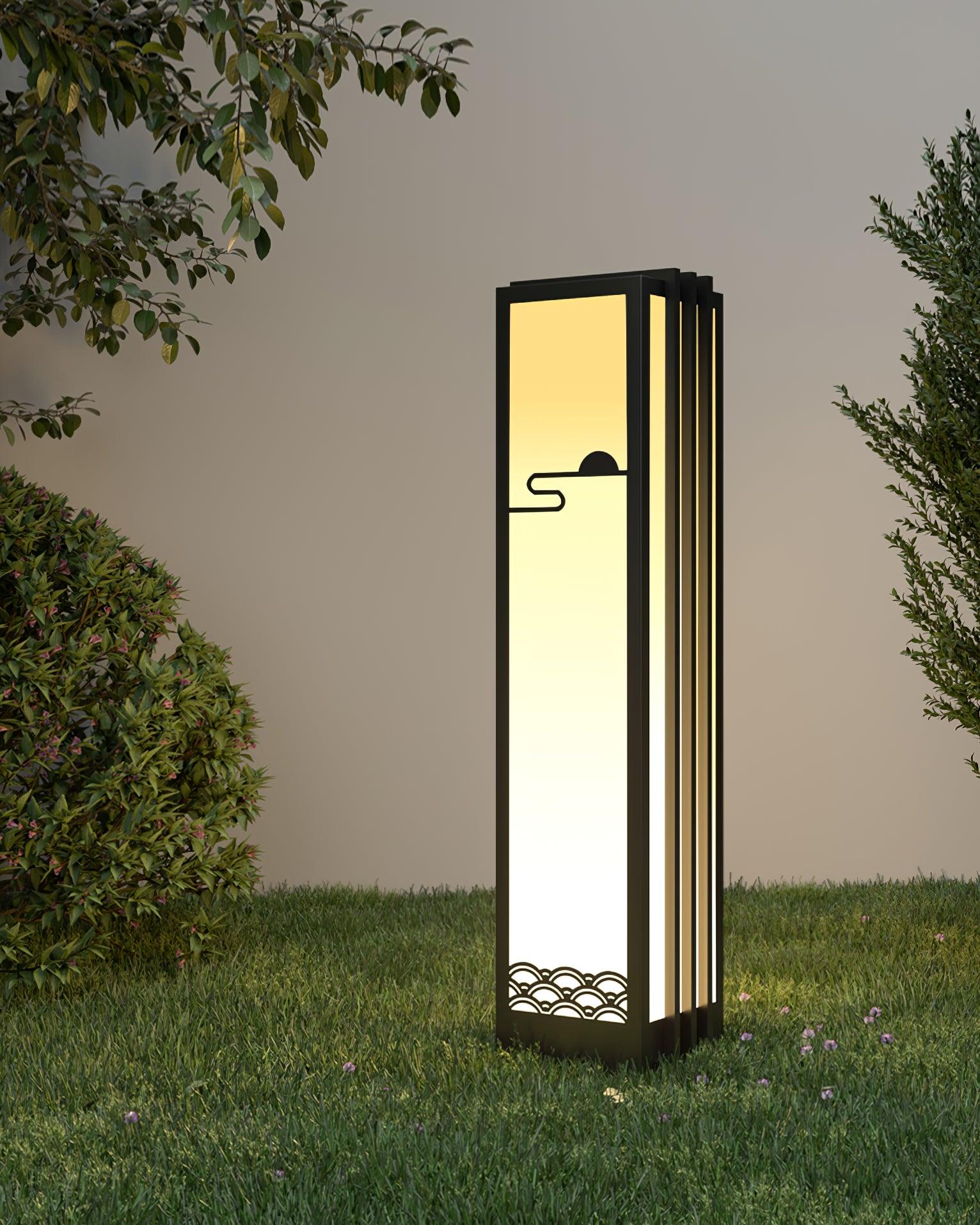 Tall black-framed lantern on lawn among shrubs and overhanging branches, with sun-and-wave front and lit side panels