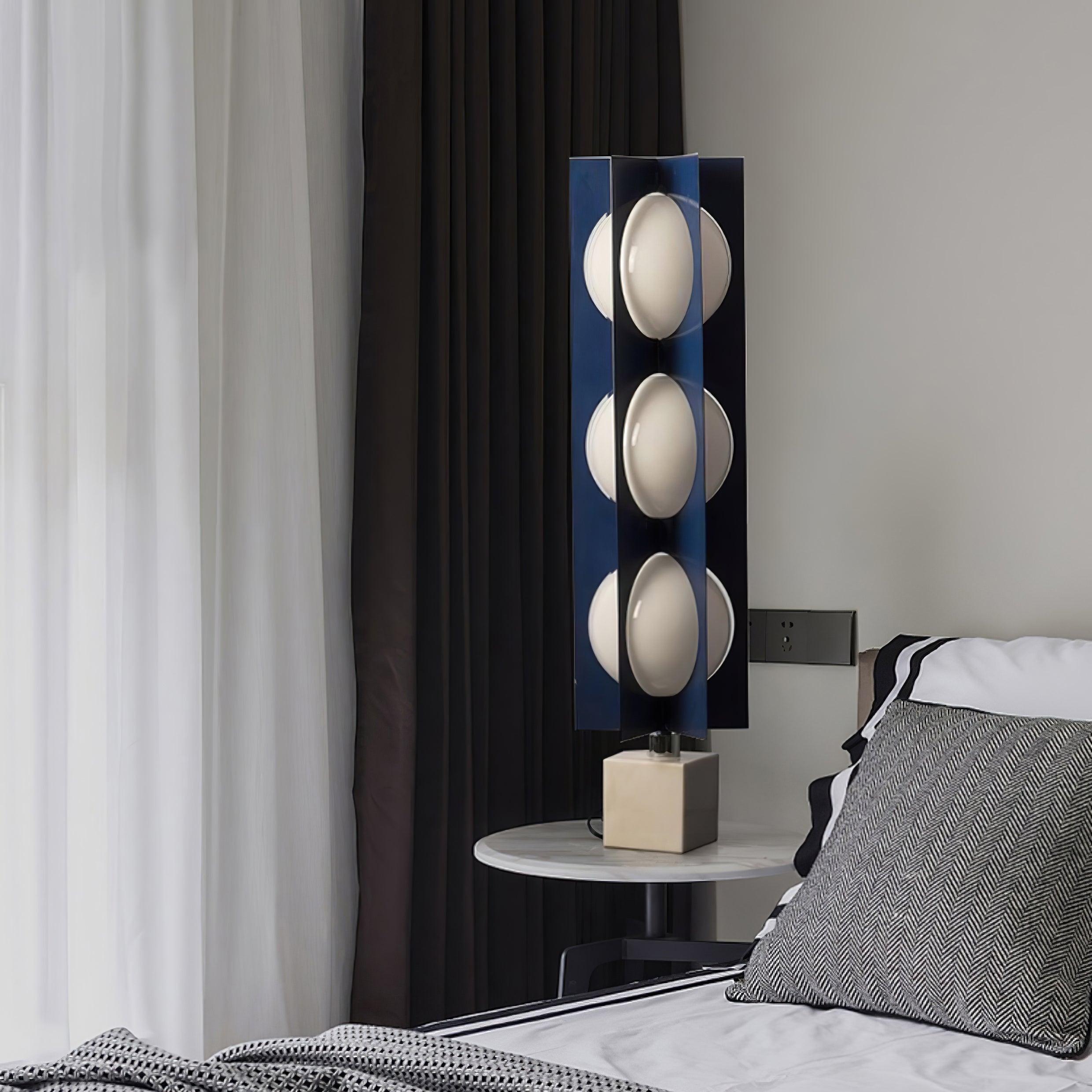 Cascade Tower on a round bedside table beside a grey patterned pillow and dark curtains