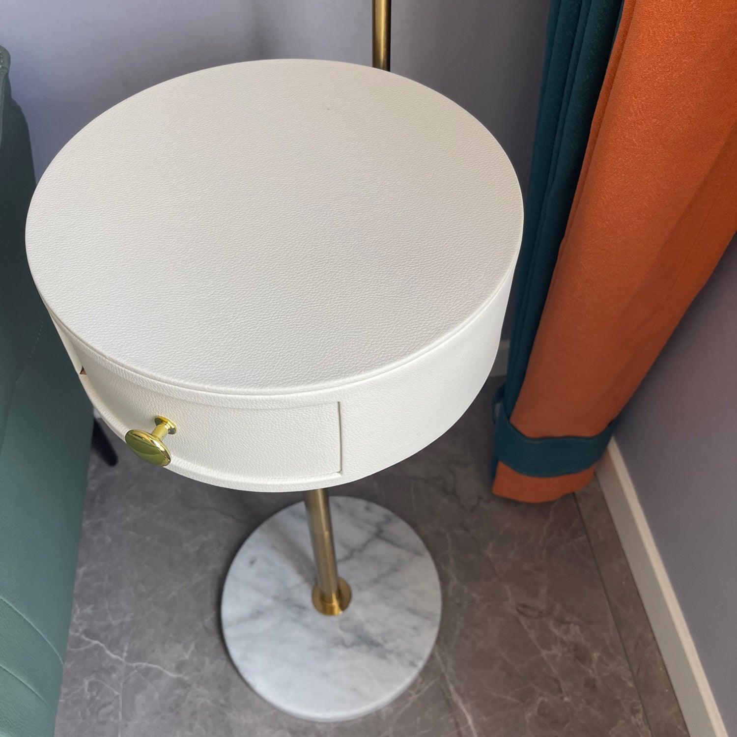 High view of white textured round table and closed curved drawer front with gold knob, gold stem and white veined base