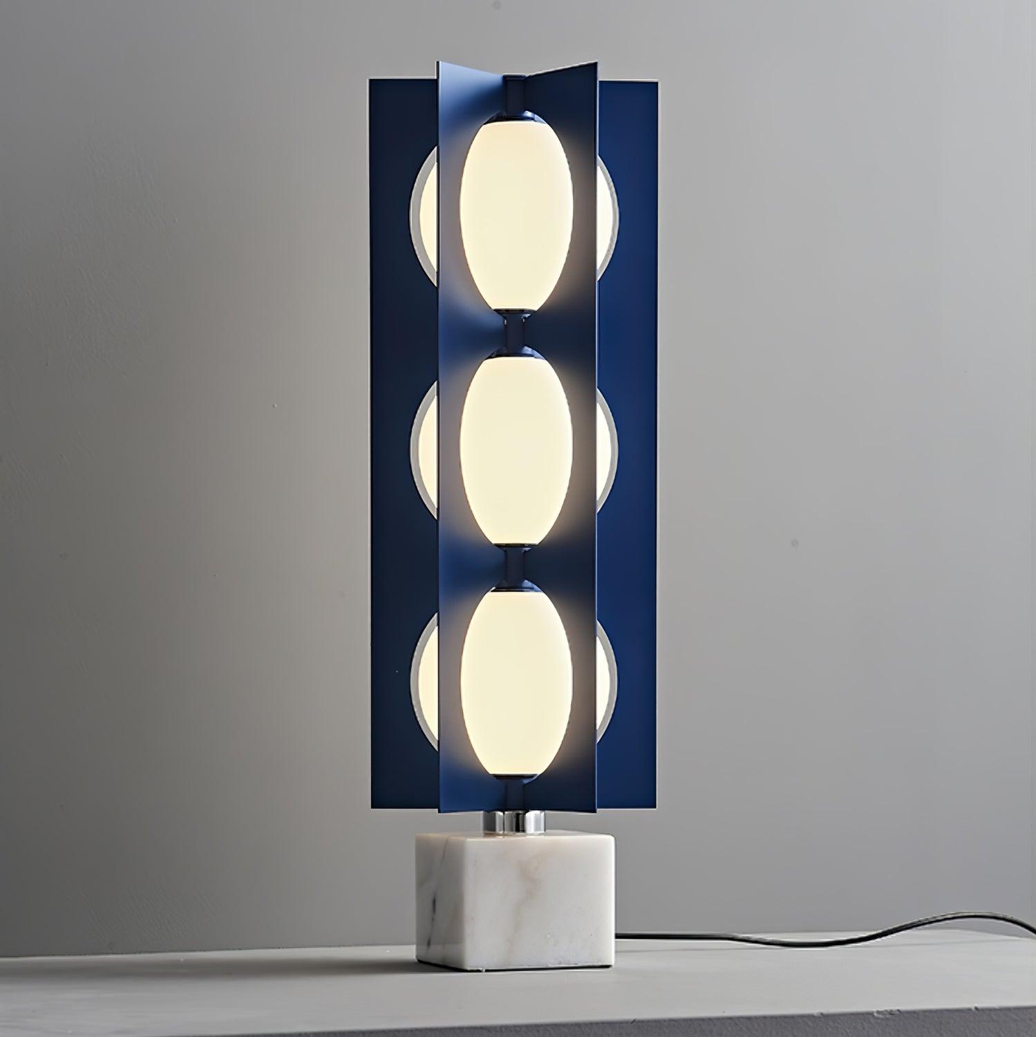 Three glowing white shade levels framed by blue metal fins above a marble base, with a trailing black lead