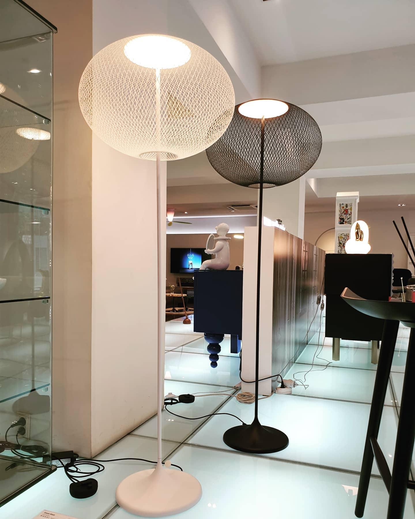 White and black mesh floor lamps in a mirrored showroom, with power cords and circular switches visible at floor level