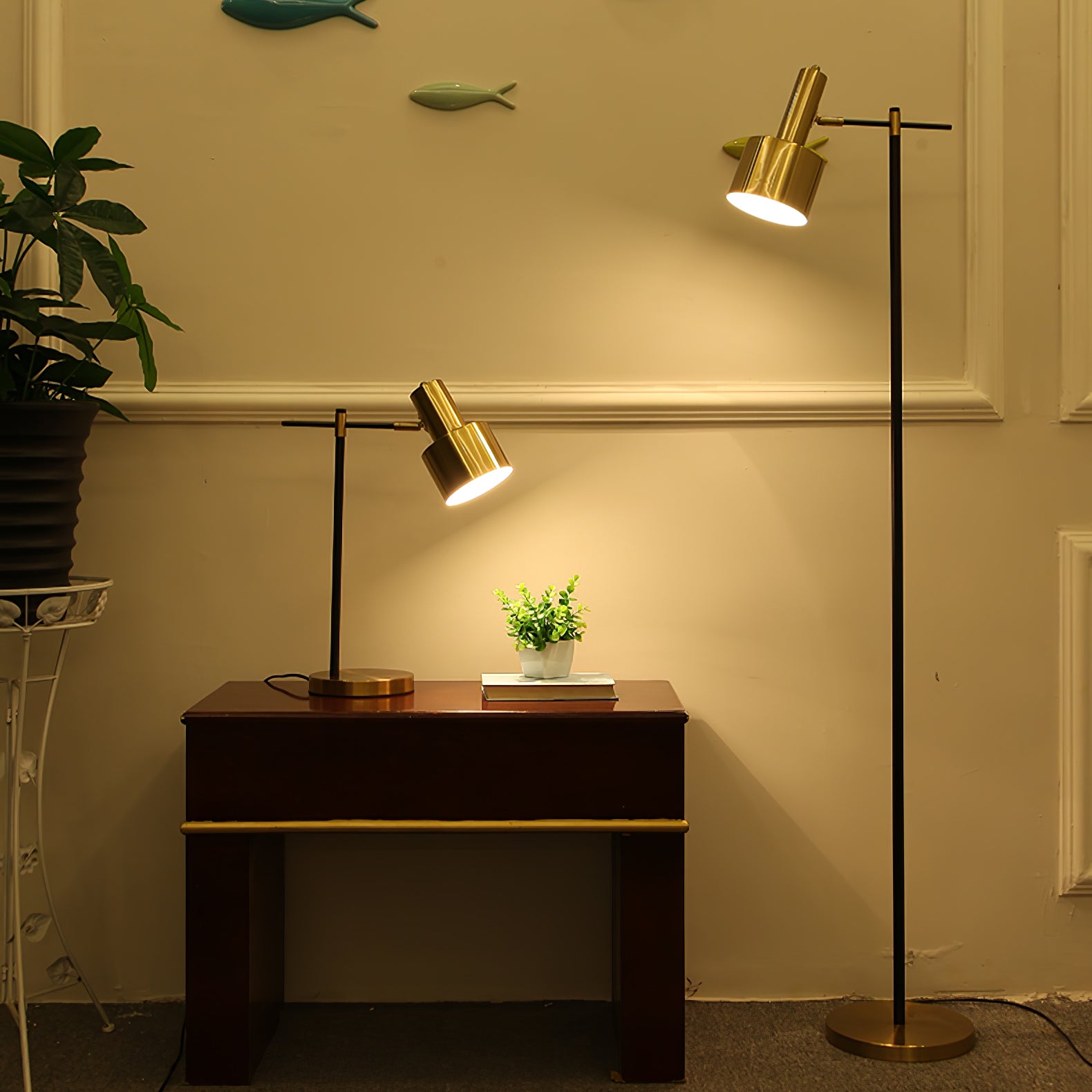 Black and gold floor lamp beside a matching table lamp on a wooden console against a yellow wall with plants