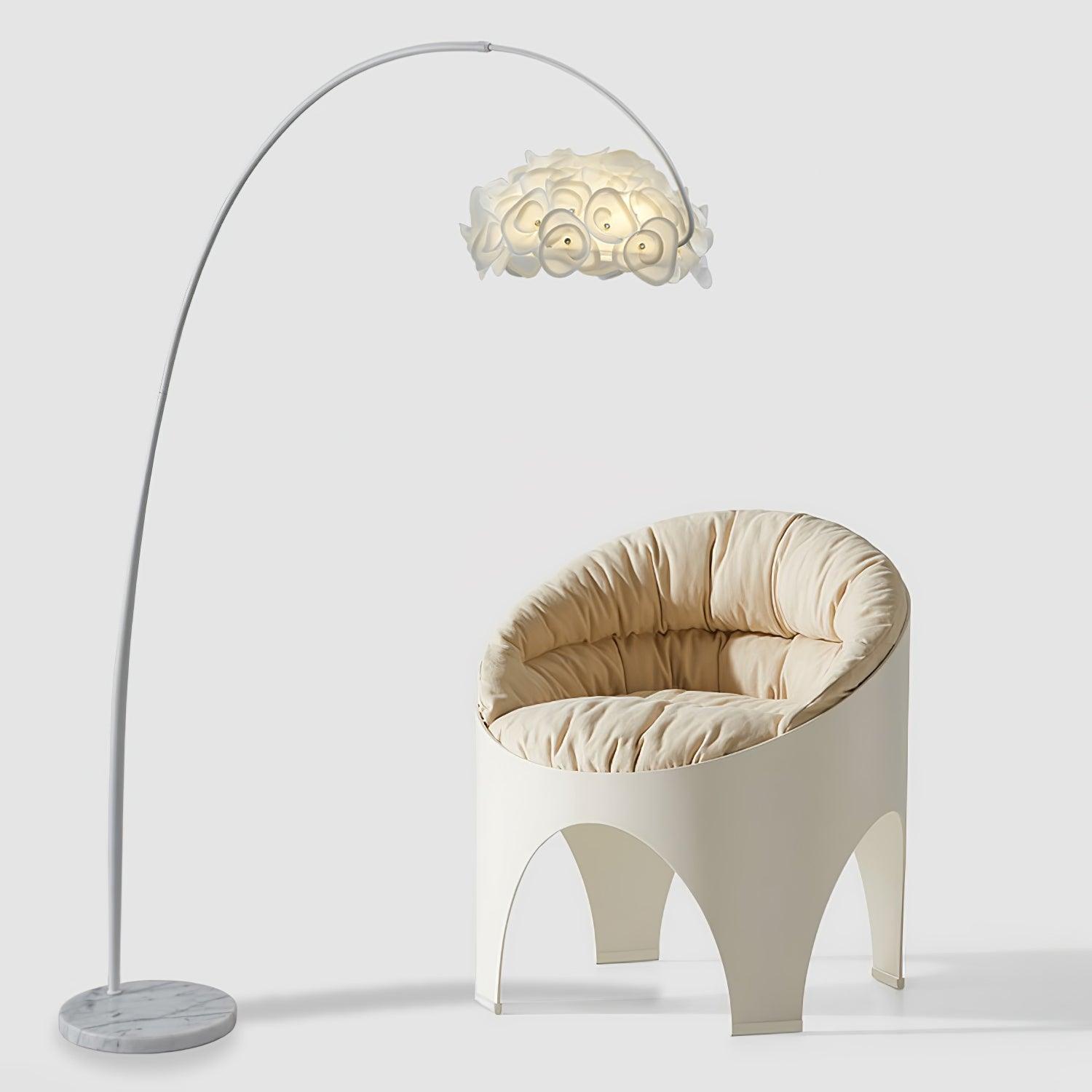 White arched petal lamp over cream upholstered sculptural chair, with gray-veined round base on pale background