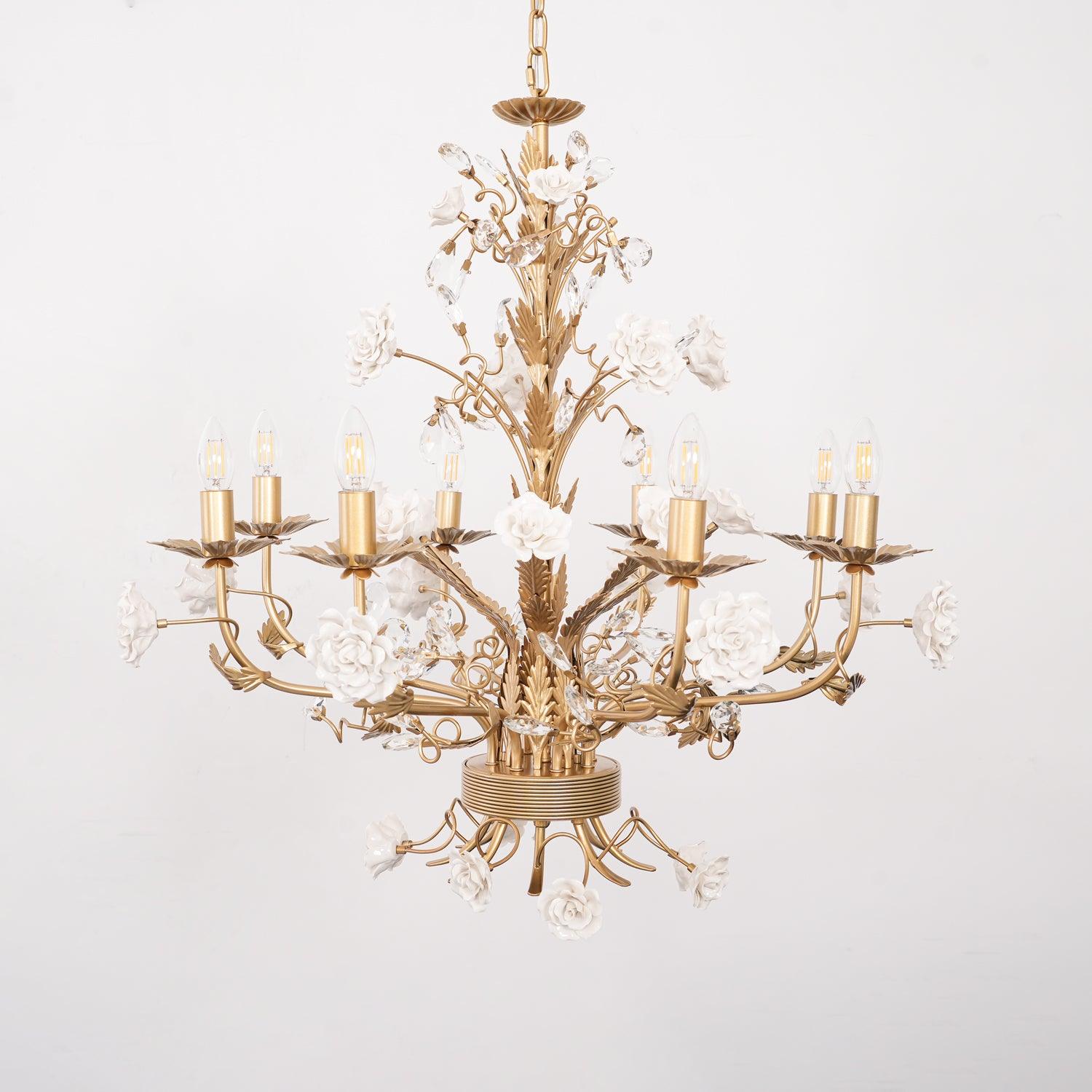 Eight-light White Rose chandelier unlit against pale wall, with gold-tone candle arms and ceramic roses beneath the lower hub