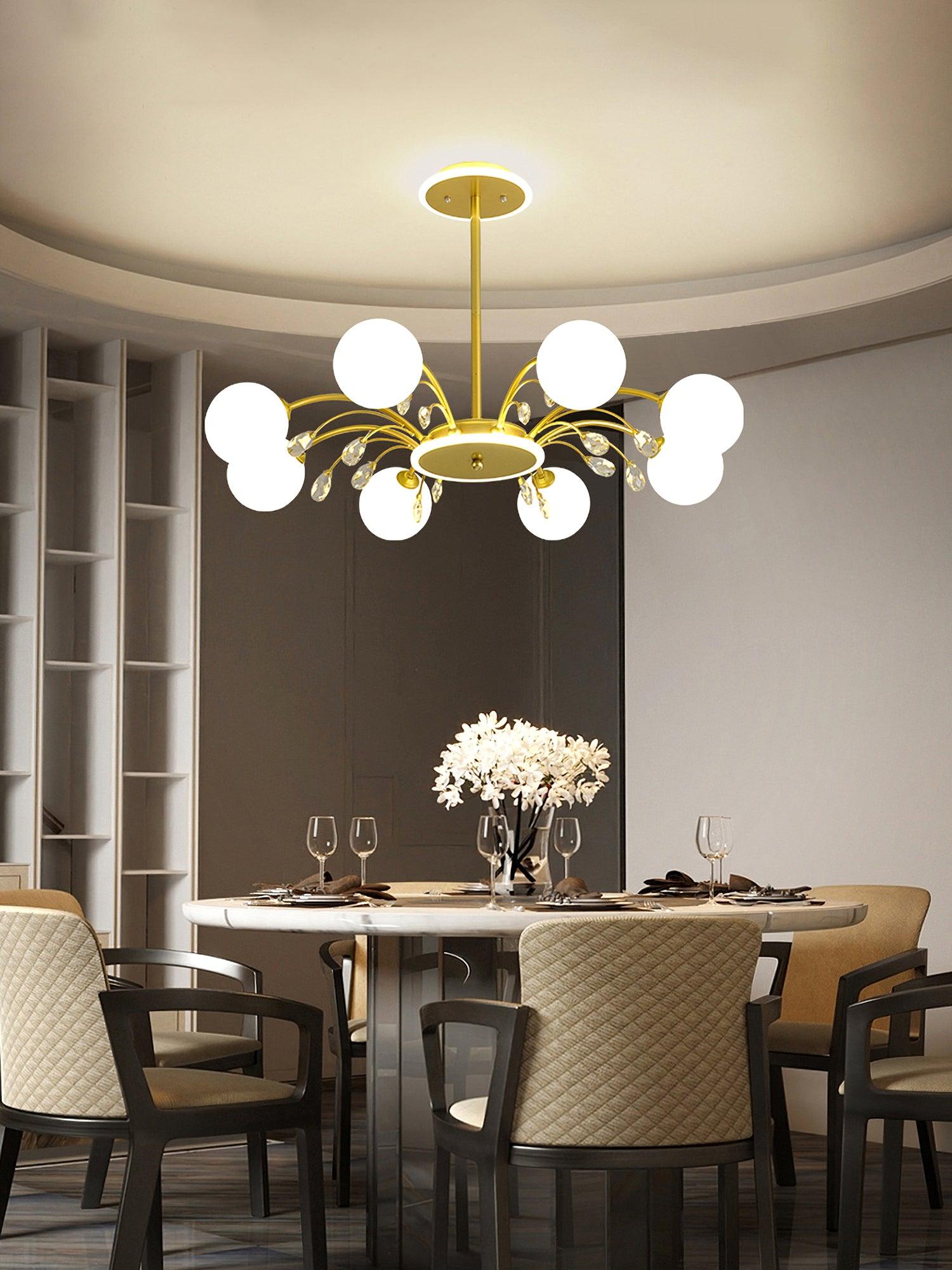 Gold globe chandelier above set dining table and beige chairs, with white flowers, circular ceiling recess and tall open shelves