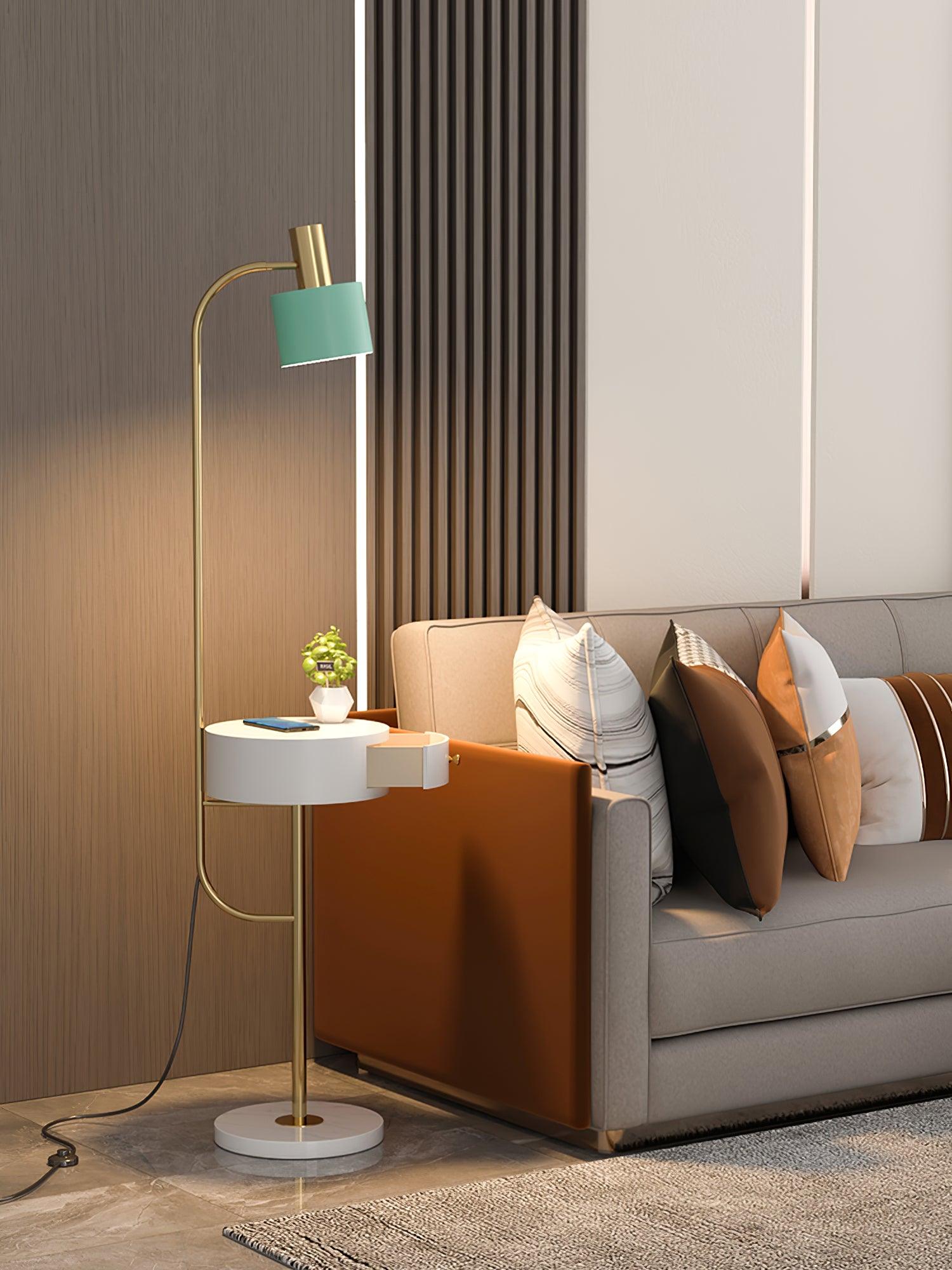 Gold lamp lit beside gray sofa and orange armrest, green shade, white open drawer table with phone and plant, white base