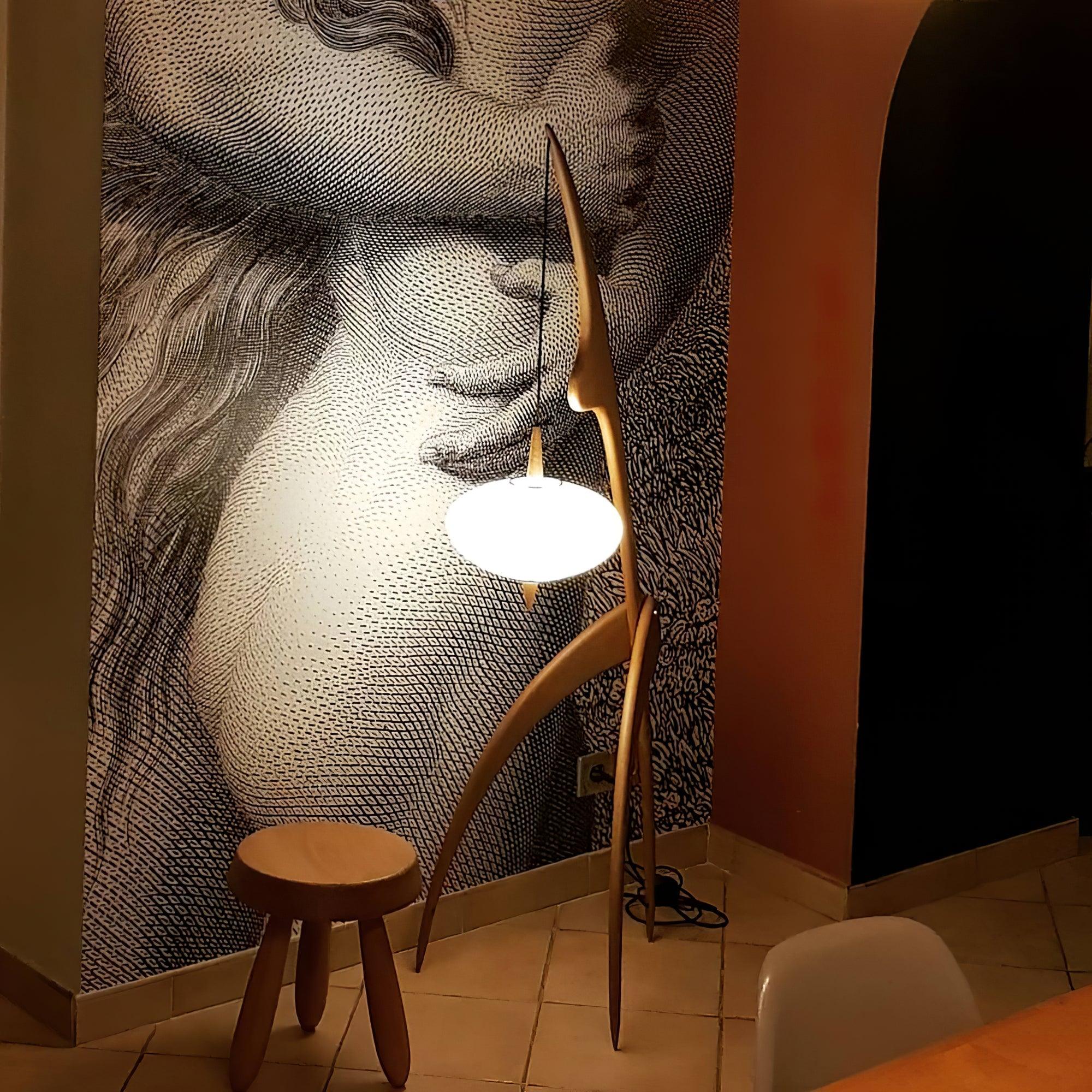 Mantis floor lamp shown beside a wooden stool and a patterned wall