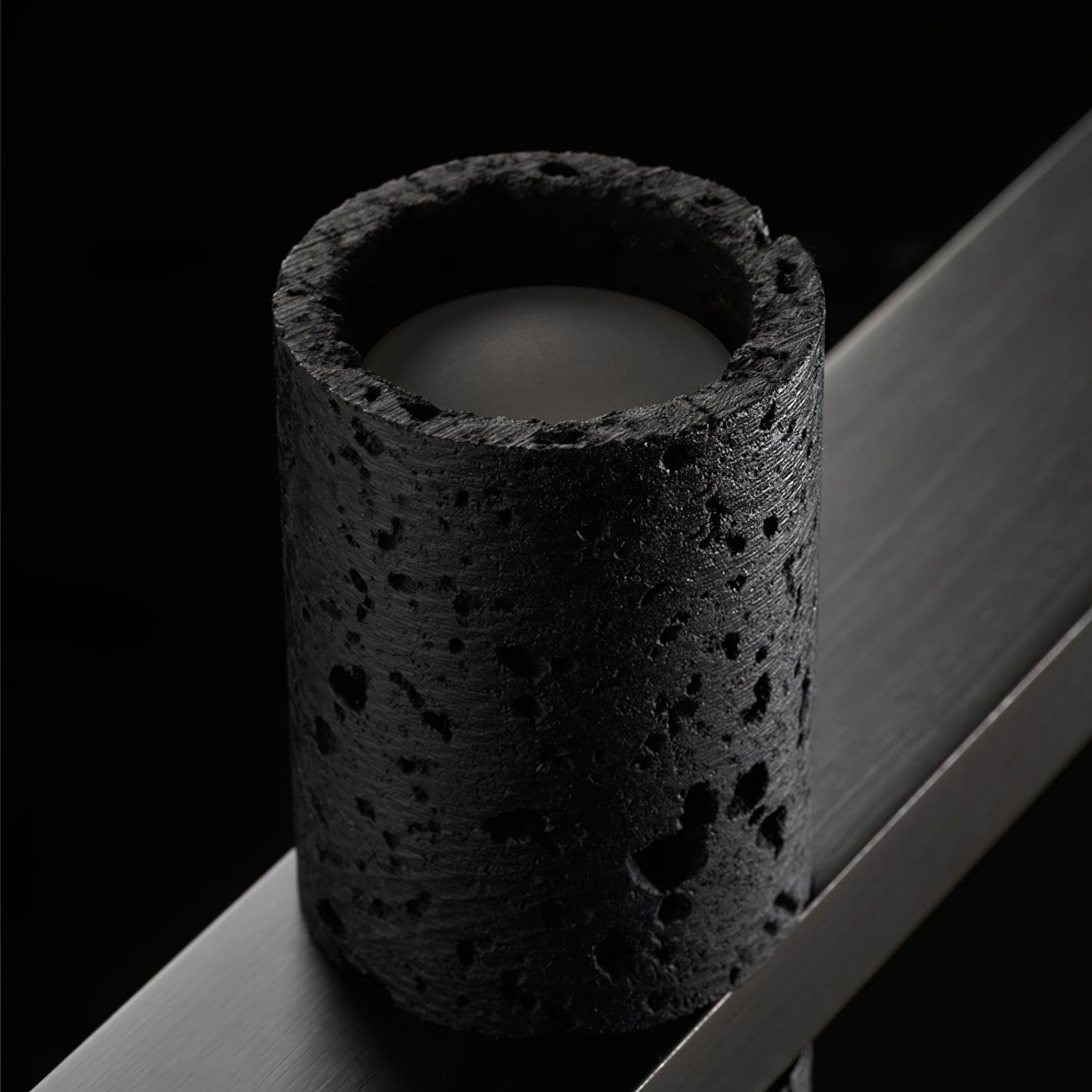 Close top view of porous black cylinder with pale recessed circular face inside opening and smooth black bar across its centre.