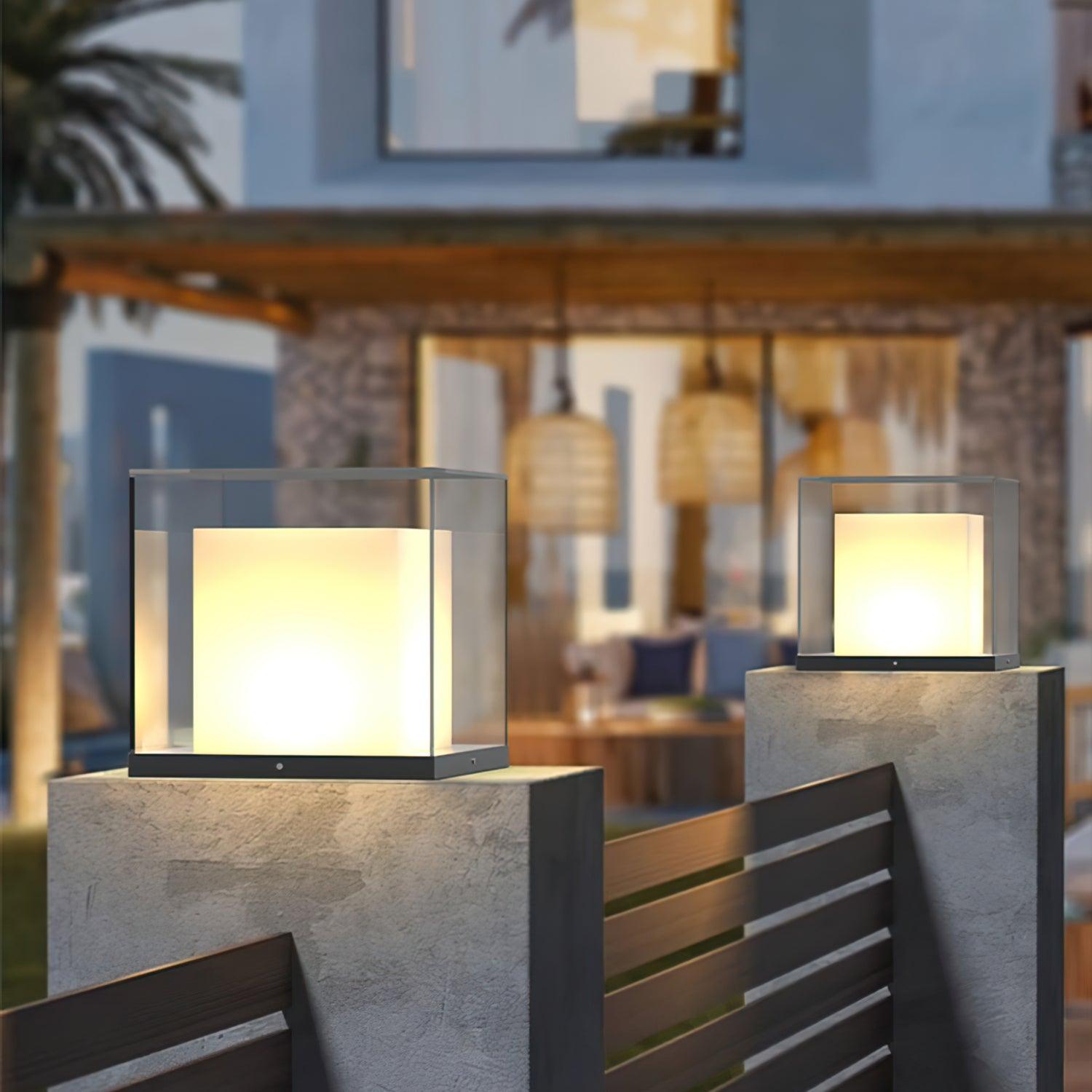 Pair of glass cube lights on entrance pillars above a wide slatted gate, with a modern house and trees behind